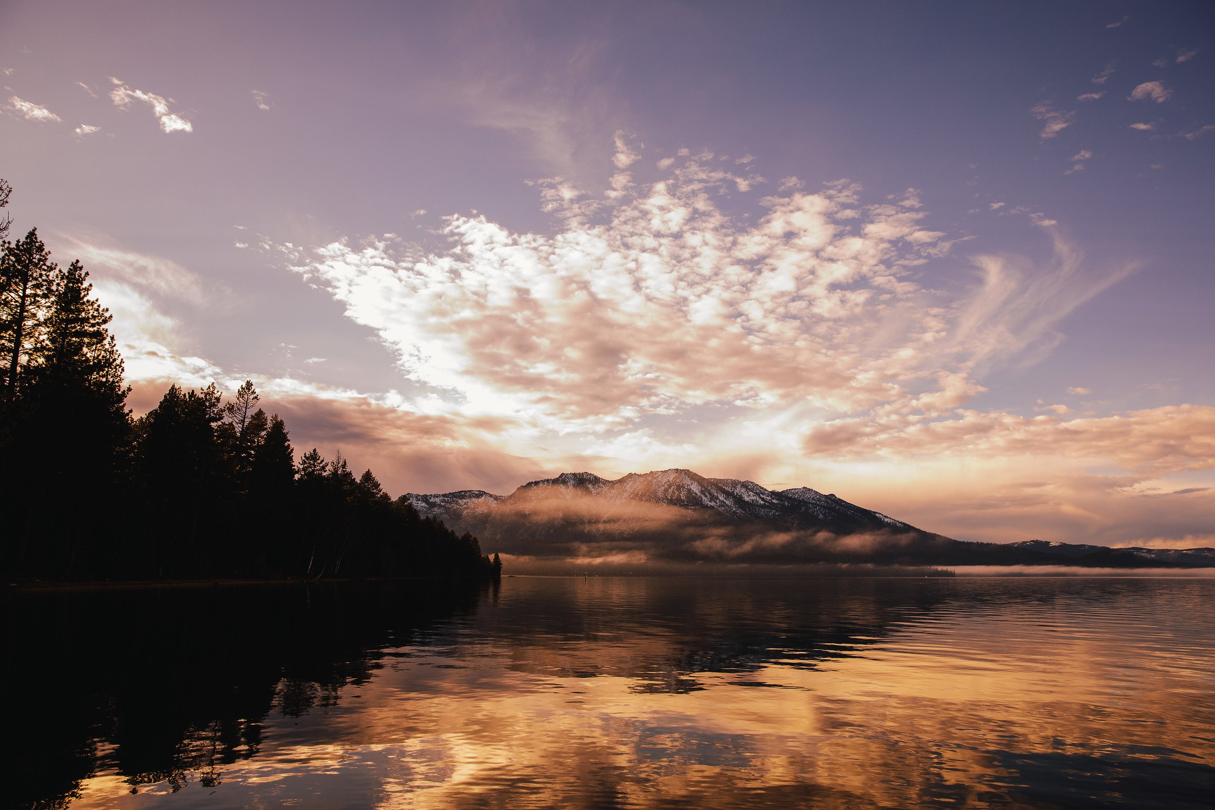 Lake Tahoe is pictured at sunset with a purple and pink sky at Valhalla Tahoe with Mt. Tallac backlit and a golden reflection. Lake Tahoe family and wedding photography by Nicky Byrnes Photography