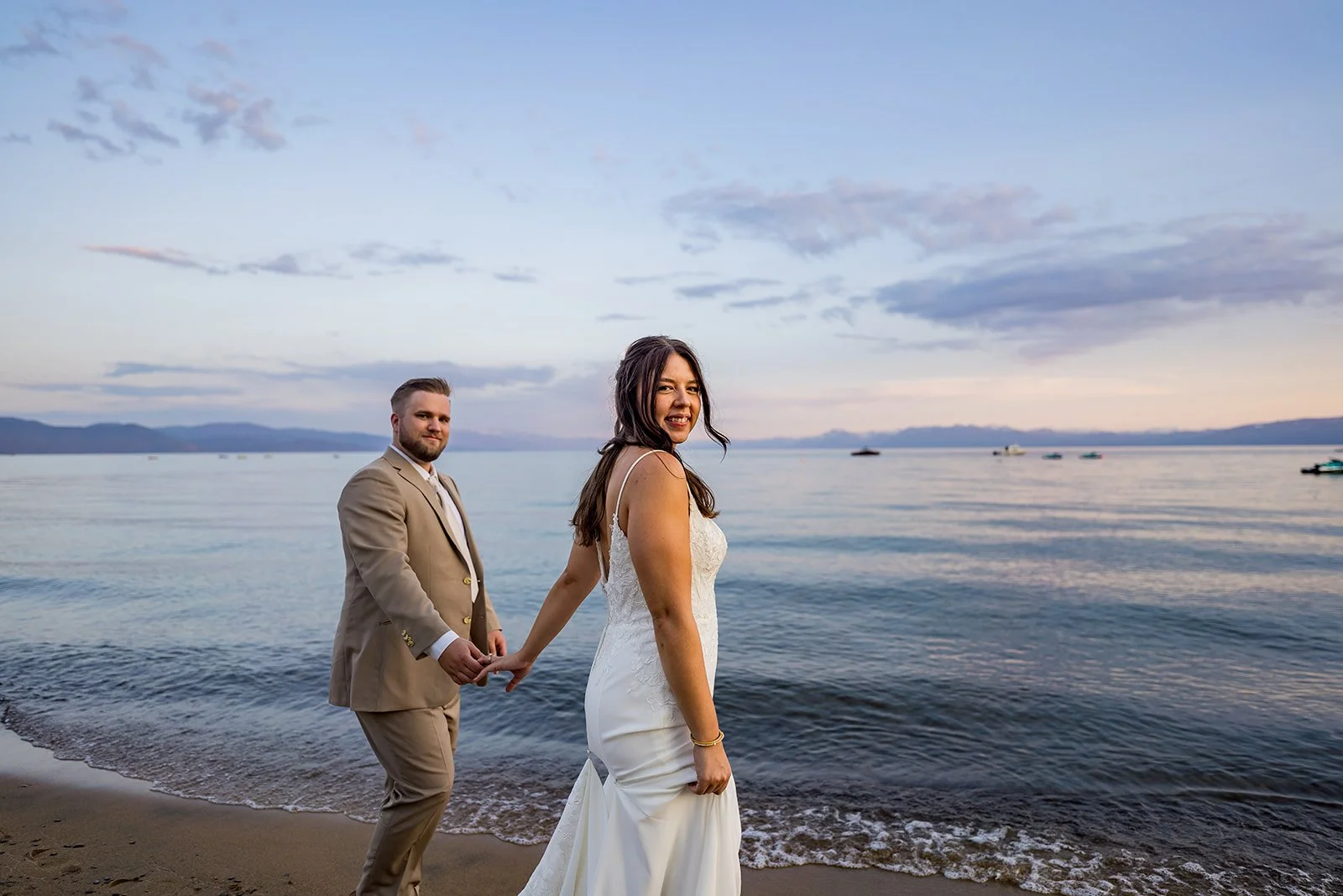 A bride and groom smile at the camera with Lake Tahoe in the background at the North Tahoe Event Center in Kings Beach, California.
