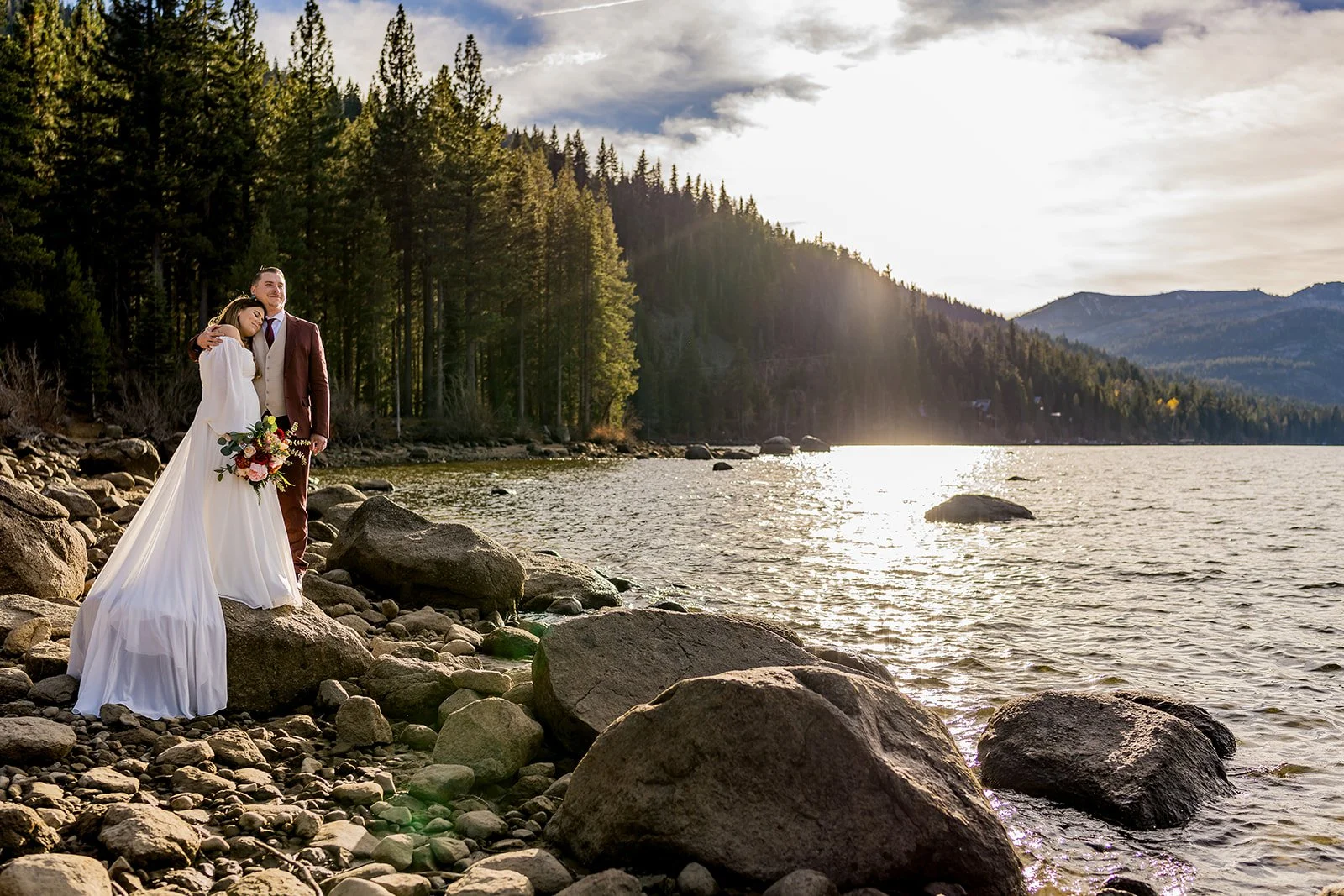 A bride is embraced by a groom wearing a maroon suit at Donner Lake photographed by Lake Tahoe wedding photographer Nicky Byrnes Photography