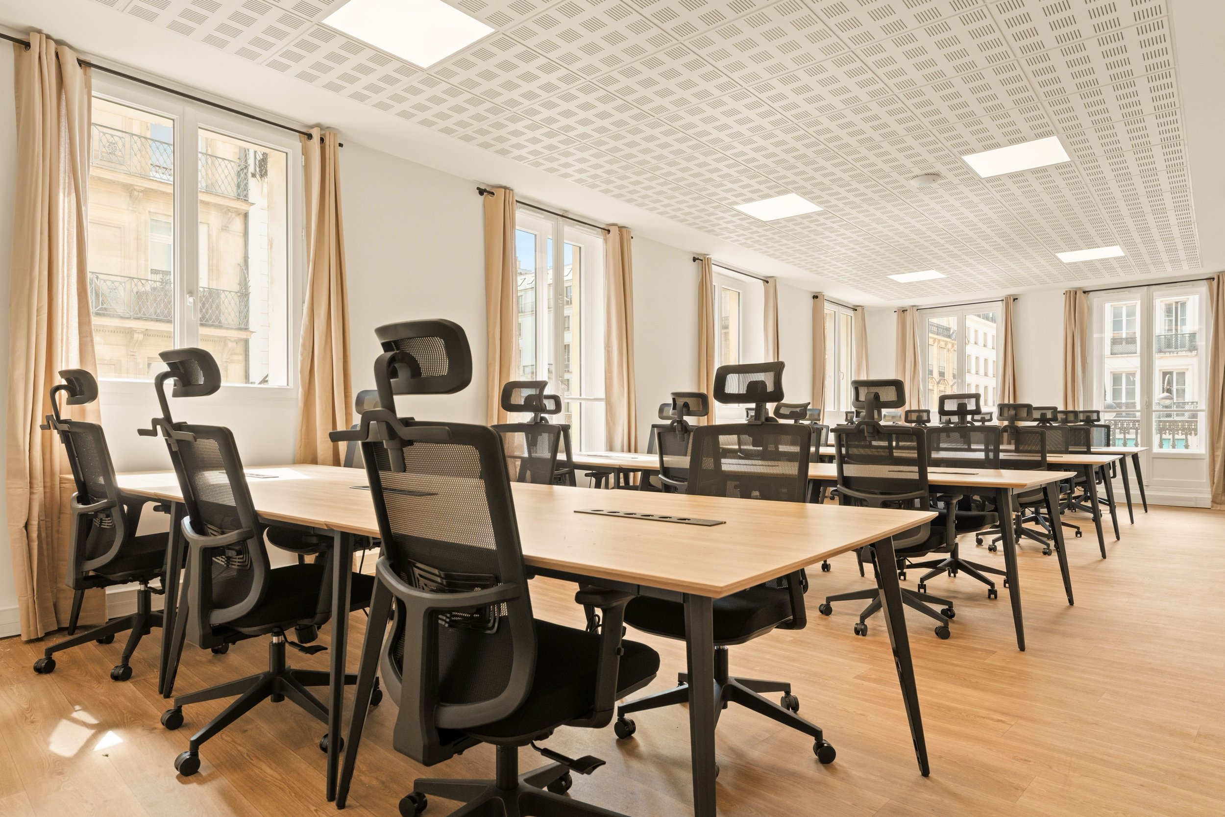 Grand open space lumineux du bureau Grands Boulevards avec des tables, des chaises ergonomiques et de grandes fenêtres