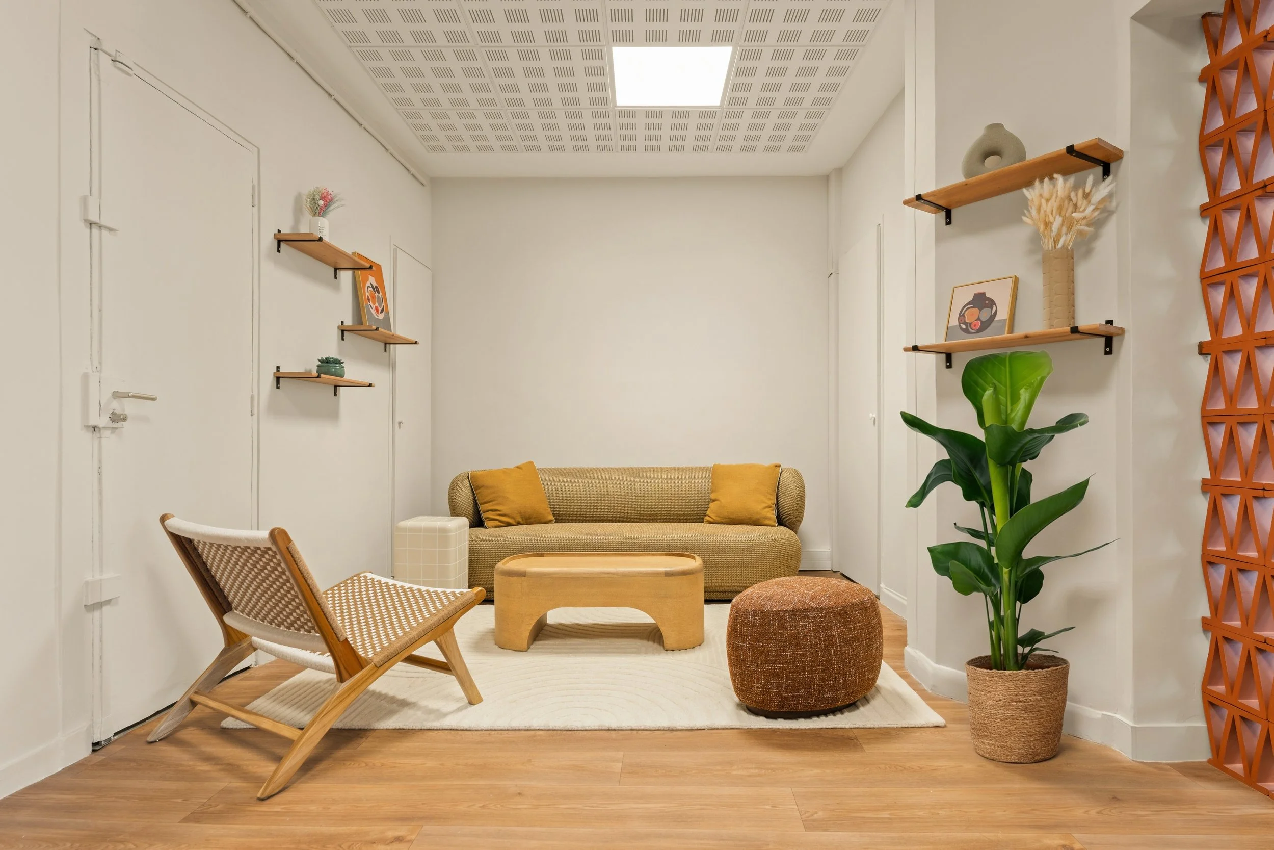 Salon minimaliste et moderne avec meubles beige et blanc, étagère en bois, table basse avec vase de fleurs, fauteuil confortable, et espace de cabine de thérapie ou de consultation en forme d'arc.