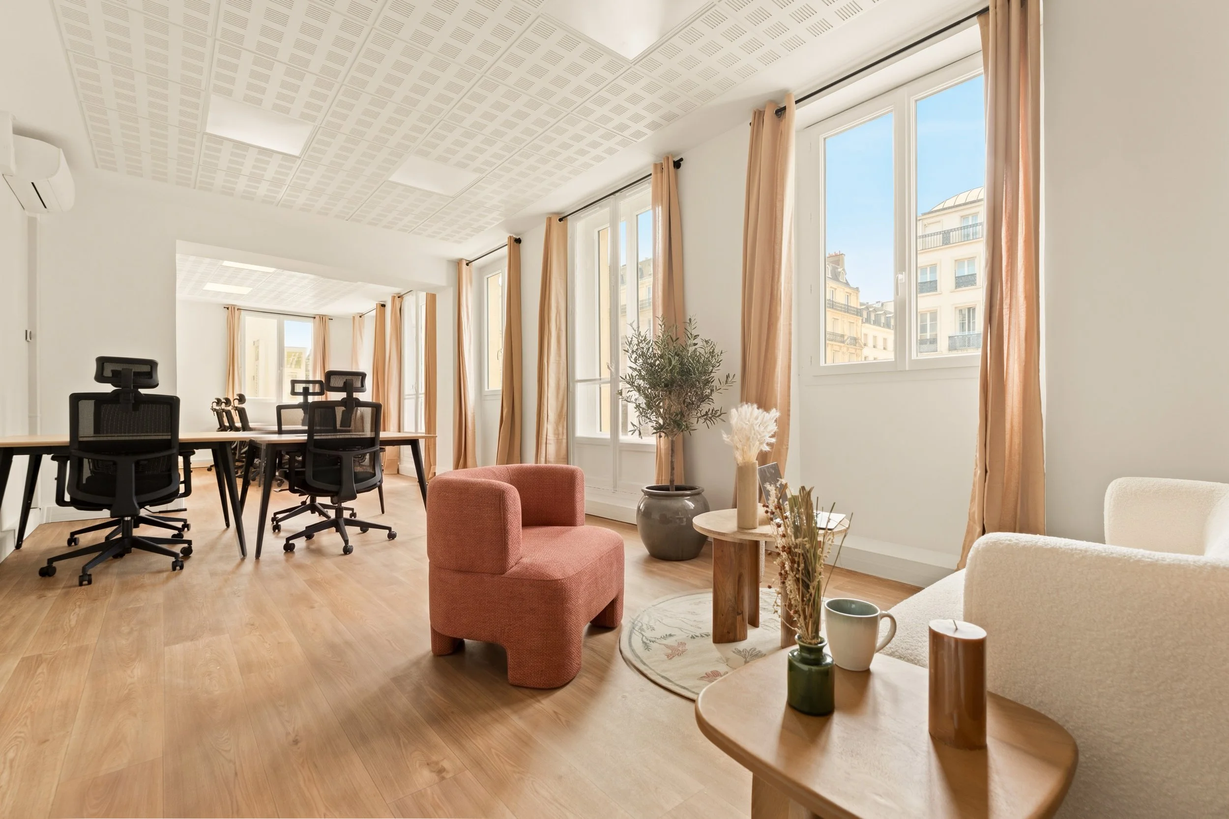 Une salle de réunion lumineuse avec plusieurs tables et chaises ergonomiques, un coin salon avec fauteuils jaunes, une table basse en bois avec une plante, et des lampes suspendues en papier.