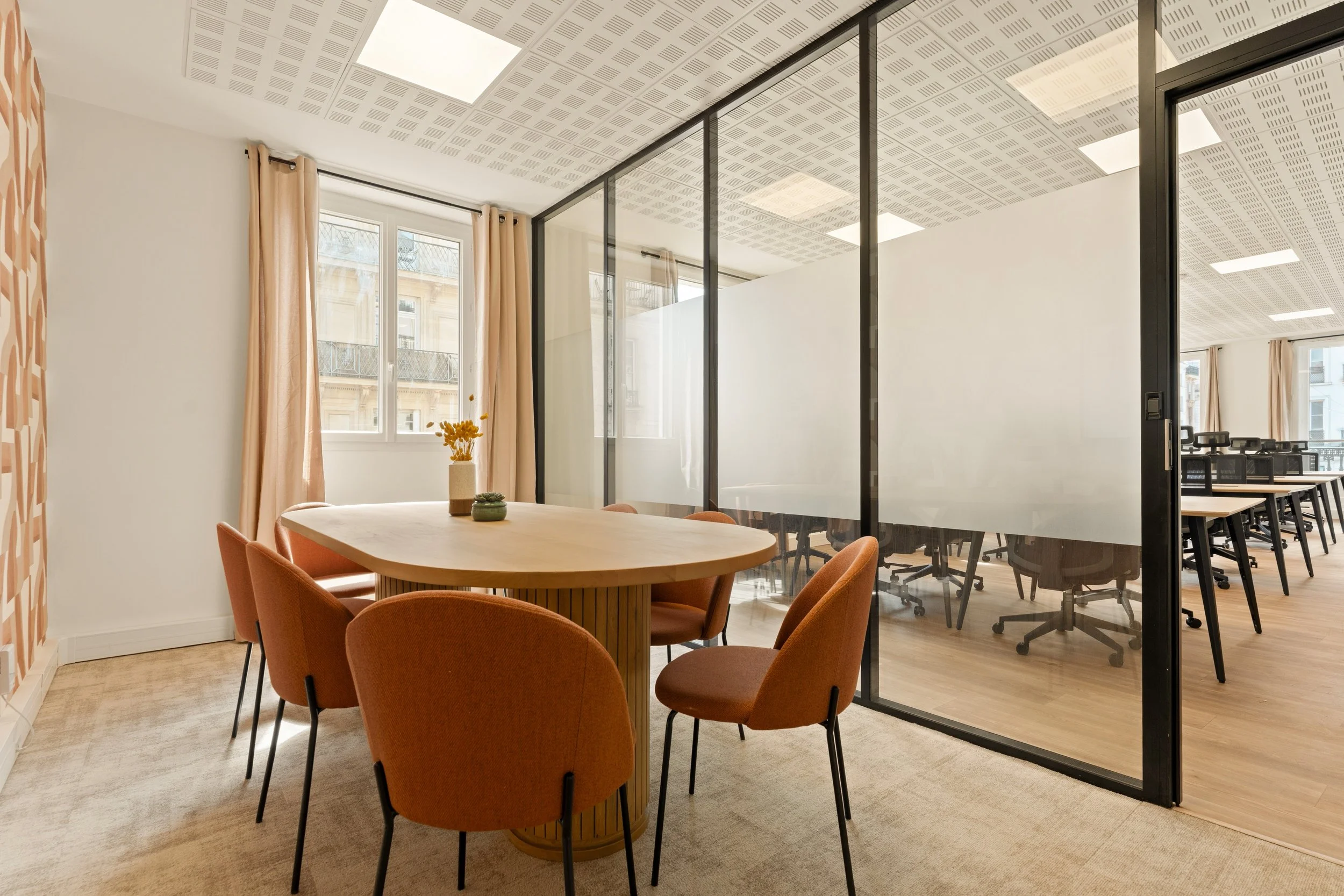 Une salle de réunion moderne avec des tables en bois et des chaises ergonomiques noires, décorée avec des œuvres d'art et des plantes
