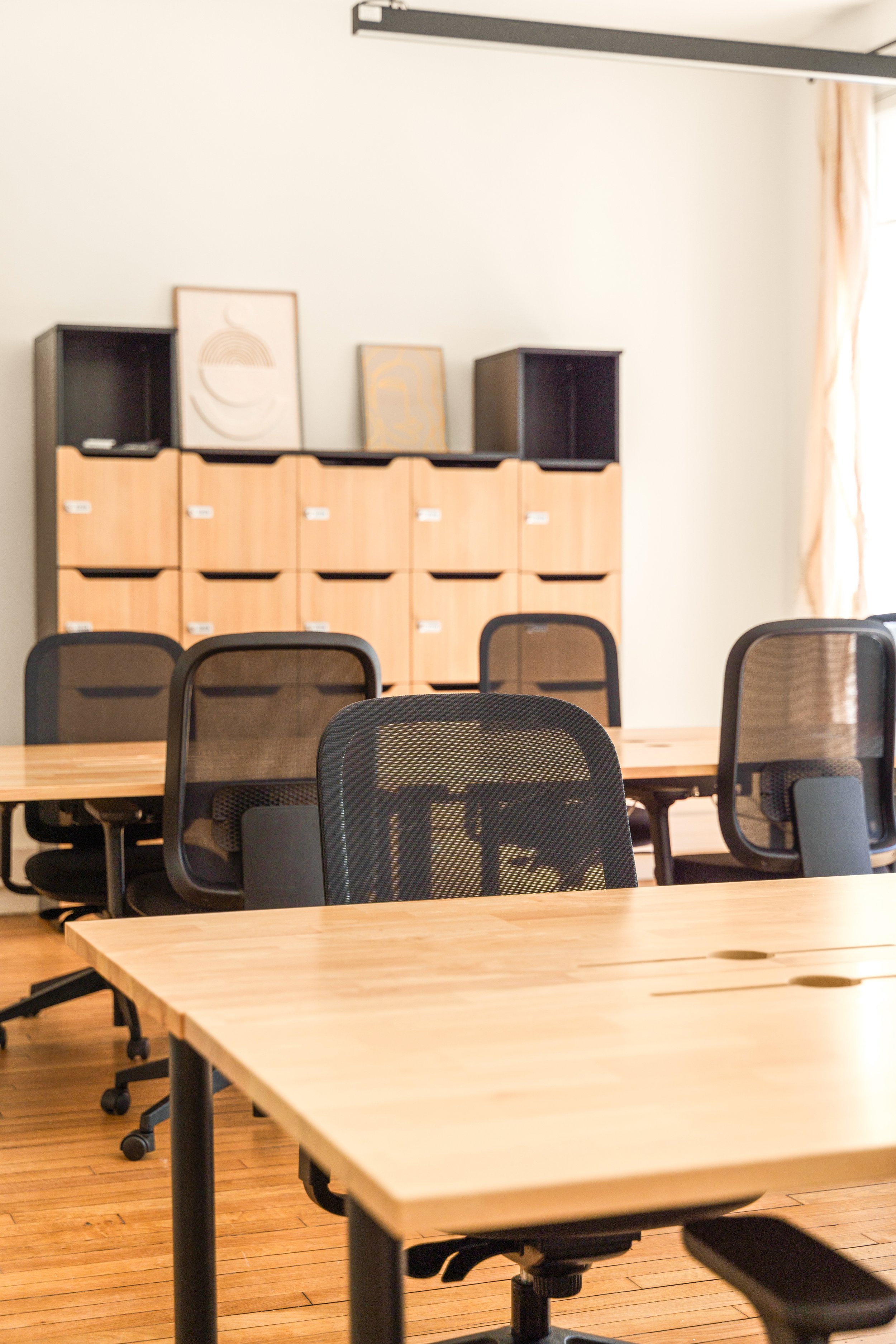 Open space du bureau Réaumur avec tables en bois, chaises noires et une armoire contenant des cadres décoratifs.