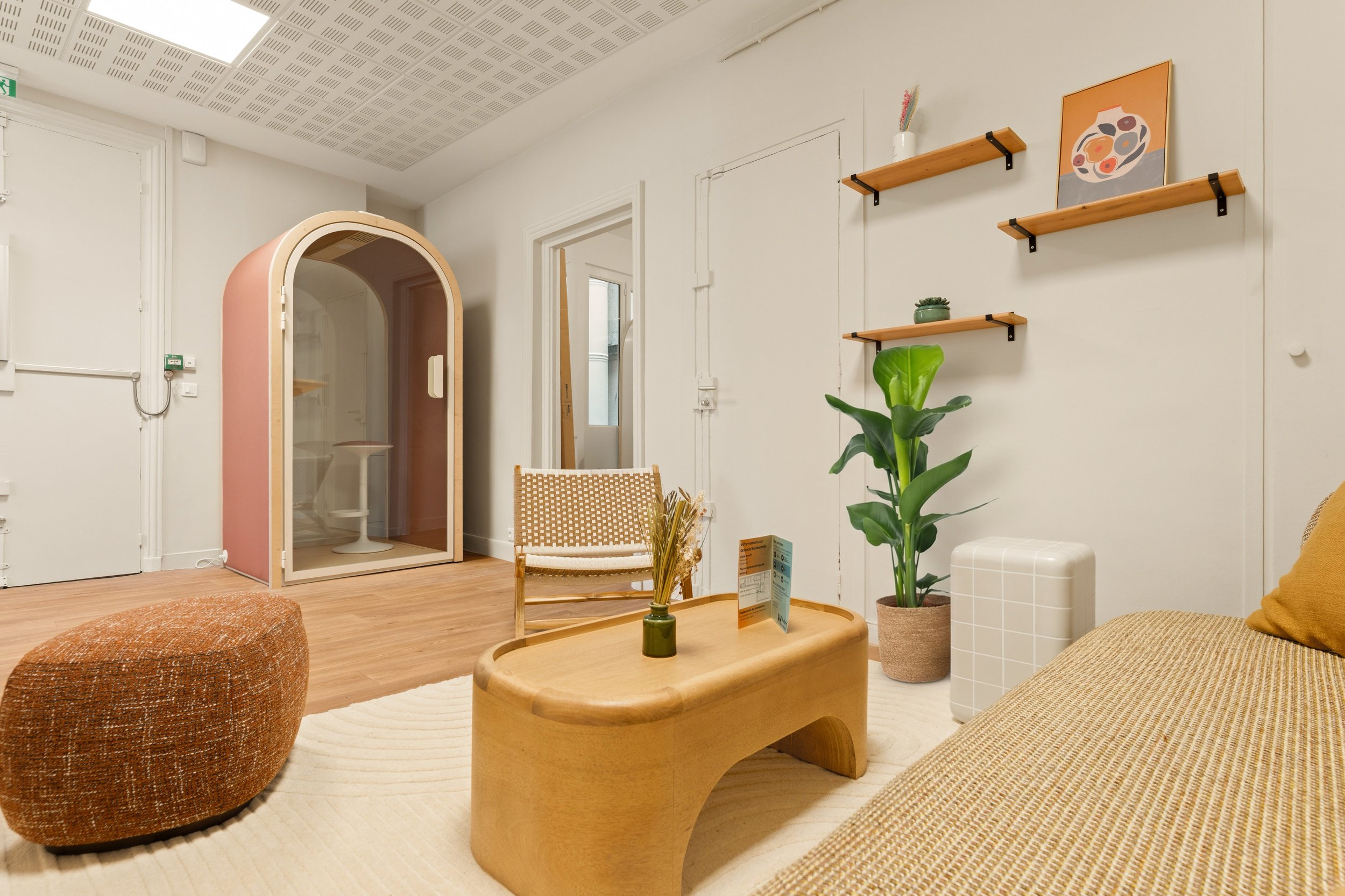 Vue intérieure d'une cuisine ouverte menant à une salle à manger avec des tables en bois et des chaises, décoration moderne avec suspension design, murs aux teintes pastel et sol en bois.