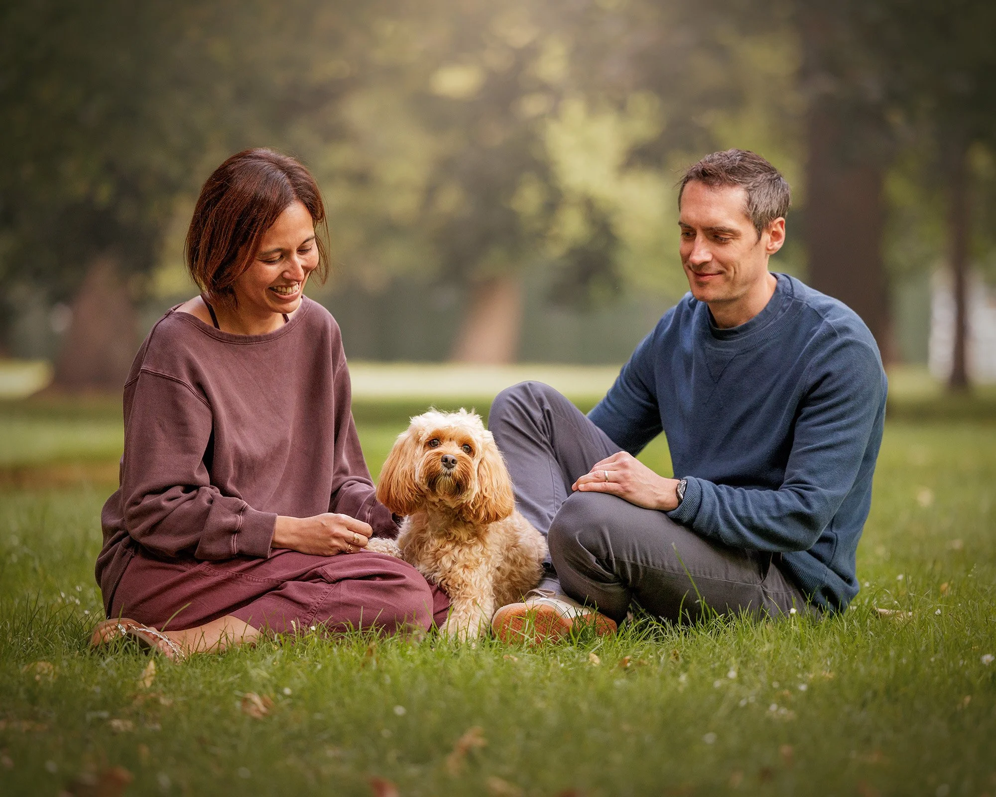 image of a couple sitting in the grass together with their poodle cross in hyde park by london dog photographer amie barron