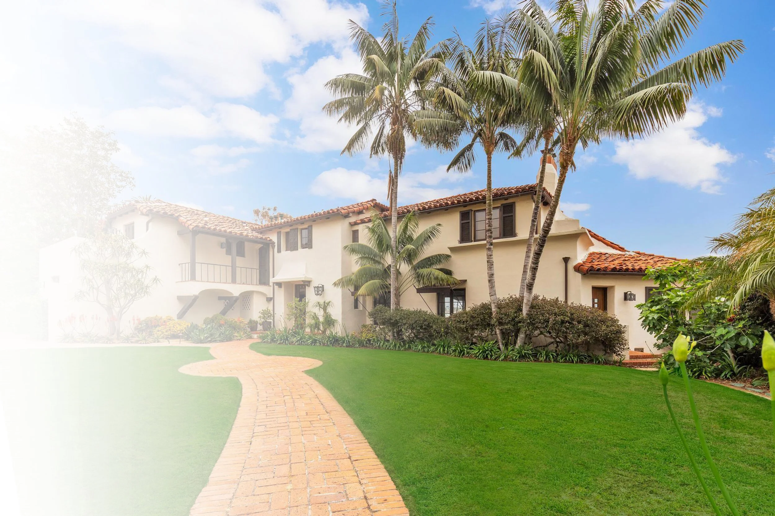 Front view of a two-story house with a dark blue front door, white exterior walls, tall green trees on both sides, and multiple windows, with steps leading to the entrance.