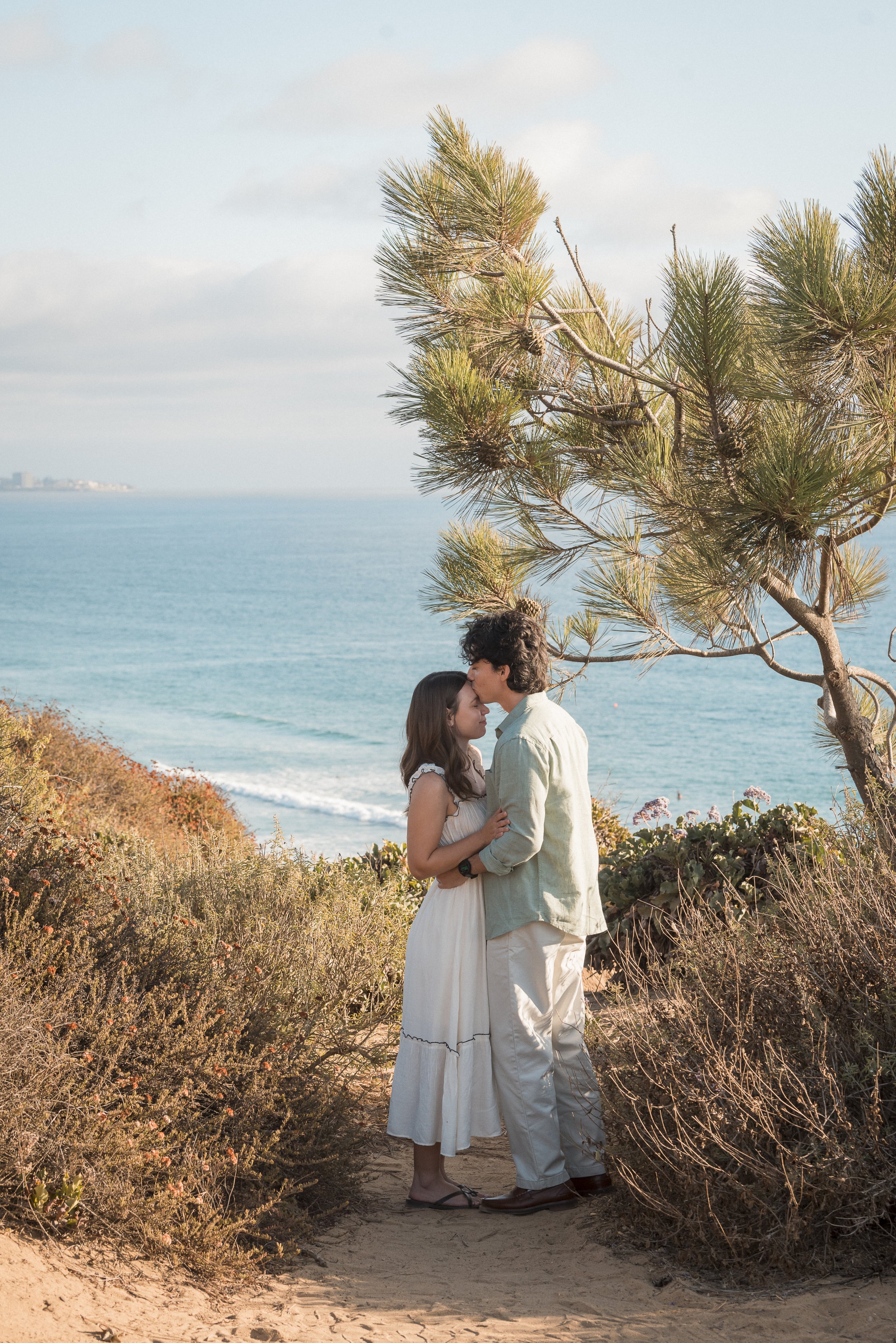 A man holding a young girl in the air at the beach with the ocean in the background.