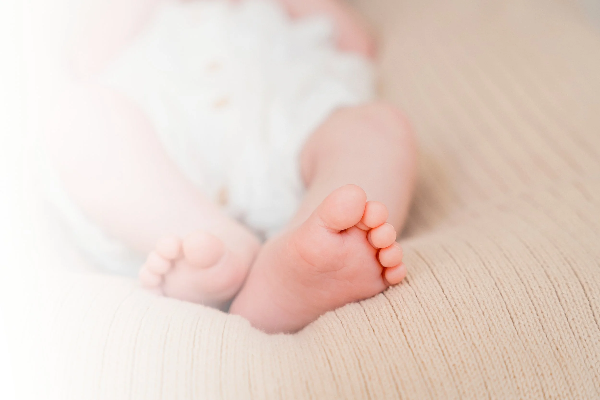 Close-up of a baby's tiny feet resting on a soft, beige surface with a blurred background.
