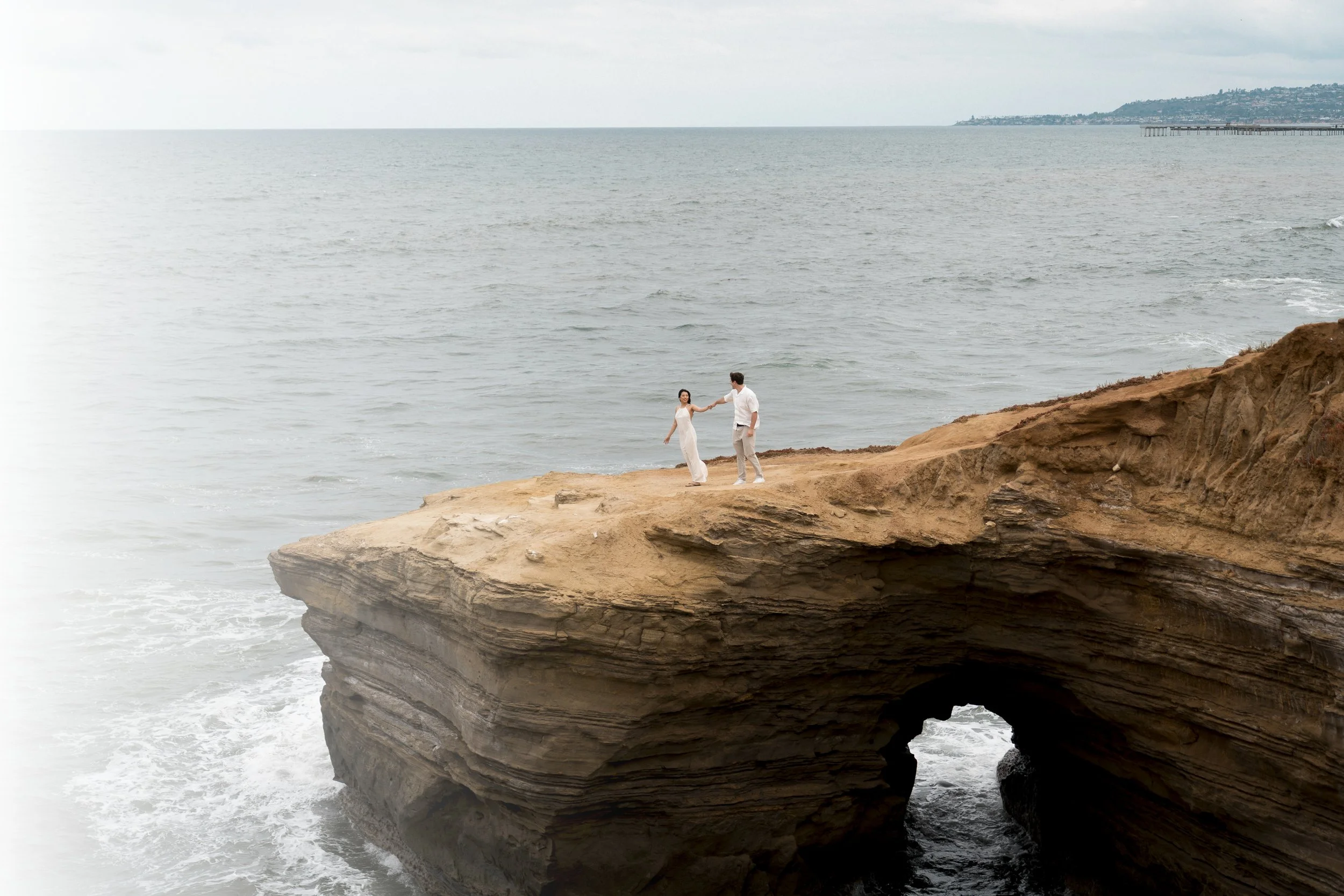 A man holding a young girl at the beach with ocean waves in the background.