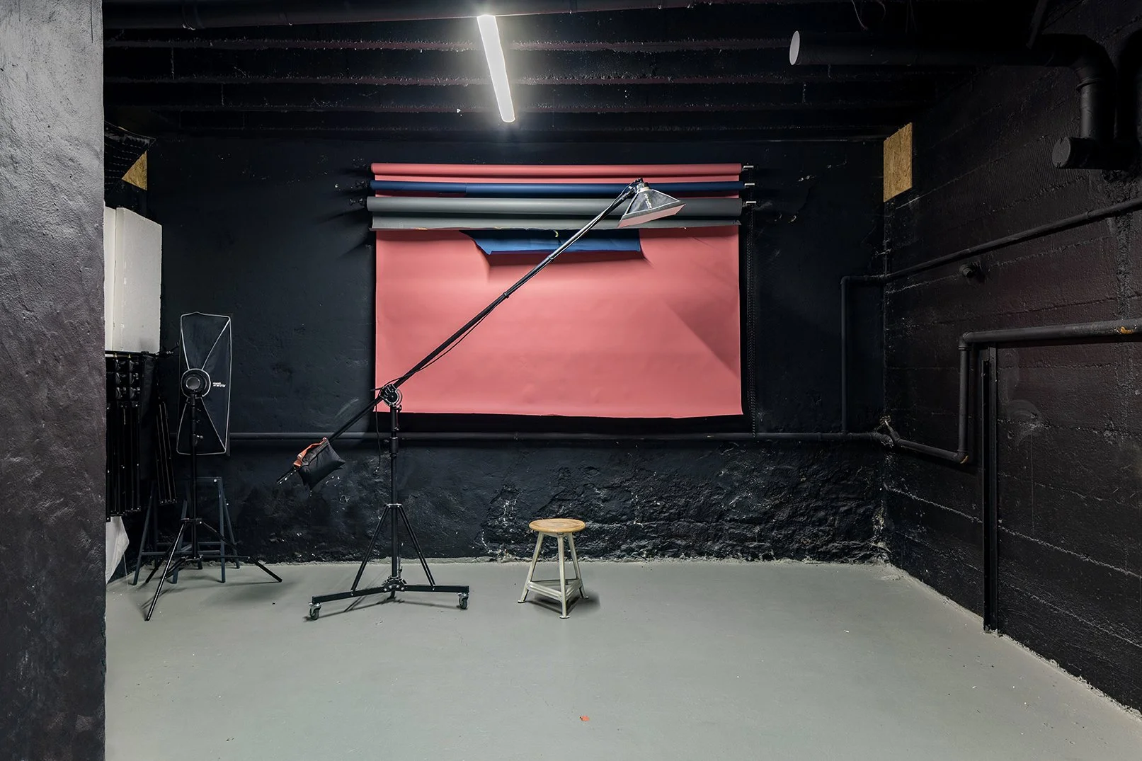 Blick ins Fotostudio von Ponderosa Coworking. Man sieht eine Hintergrundaufhängung mit unterschiedlich farbigen Papierrollen. Ausserdem zu sehen sind Blitzequipment und ein Hocker