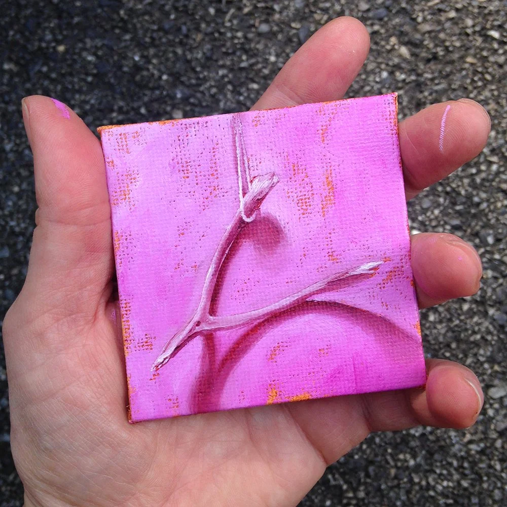 A hand holding a small, painted canvas with a pink background and a wishbone.