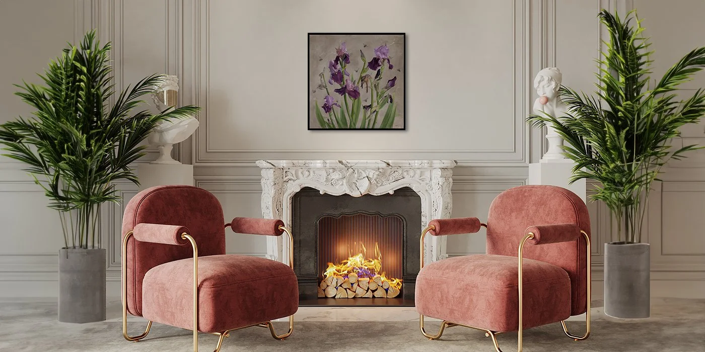 A living room with a white ornate fireplace, two pink velvet armchairs with gold armrests, two tall green plants in gray pots, and a framed floral painting of purple irises on a light gray wall.