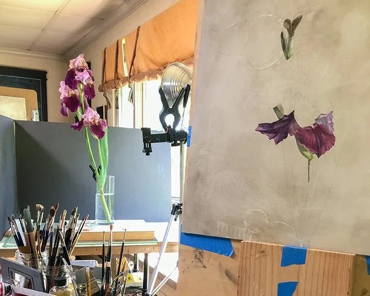 A blooming purple iris stem in a vase with Christine Mercer-Vernon's work in progress painting next to it.