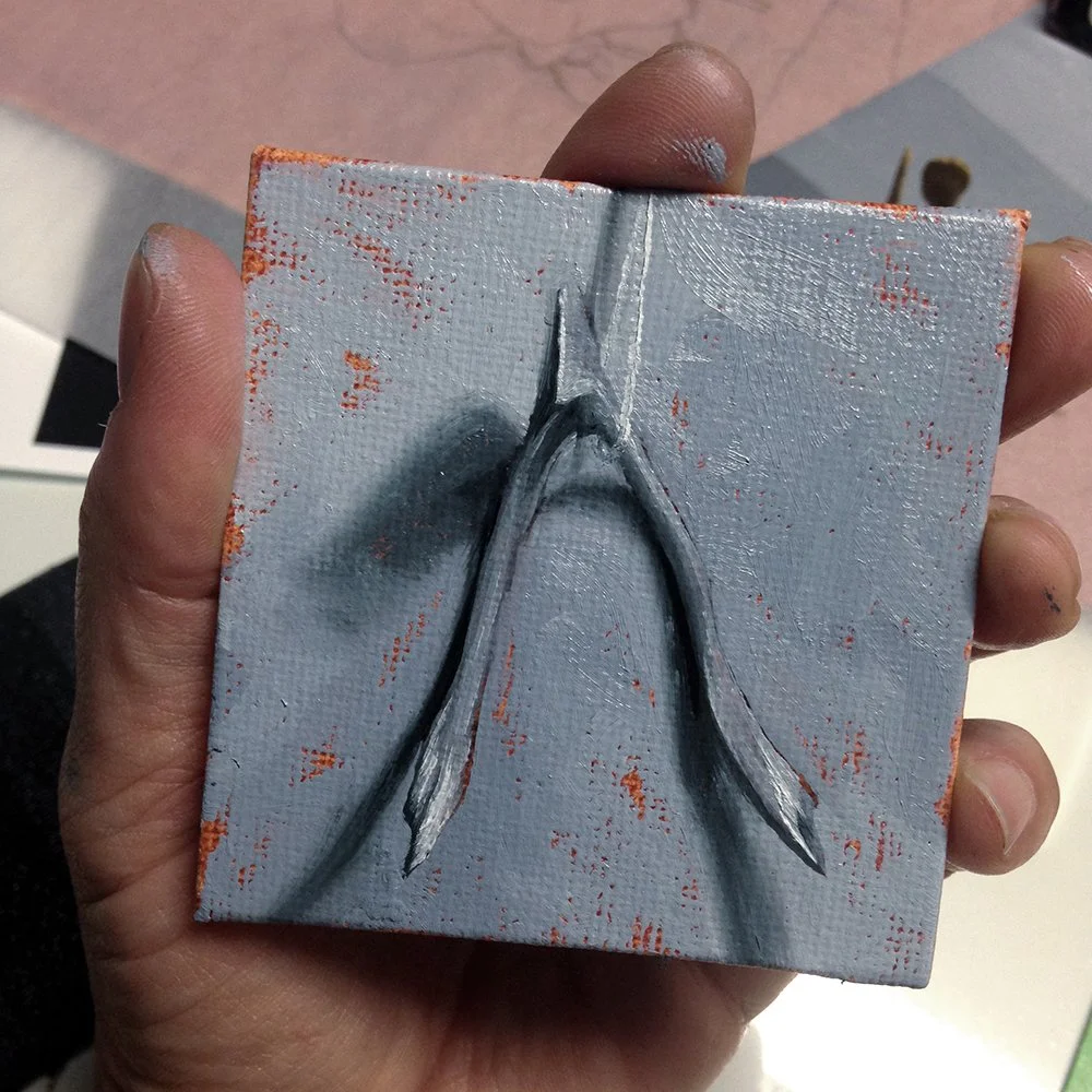 A hand holding a small canvas panel with a painting of a wishbone in shades of gray and black, against a gray background with reddish-orange accents.
