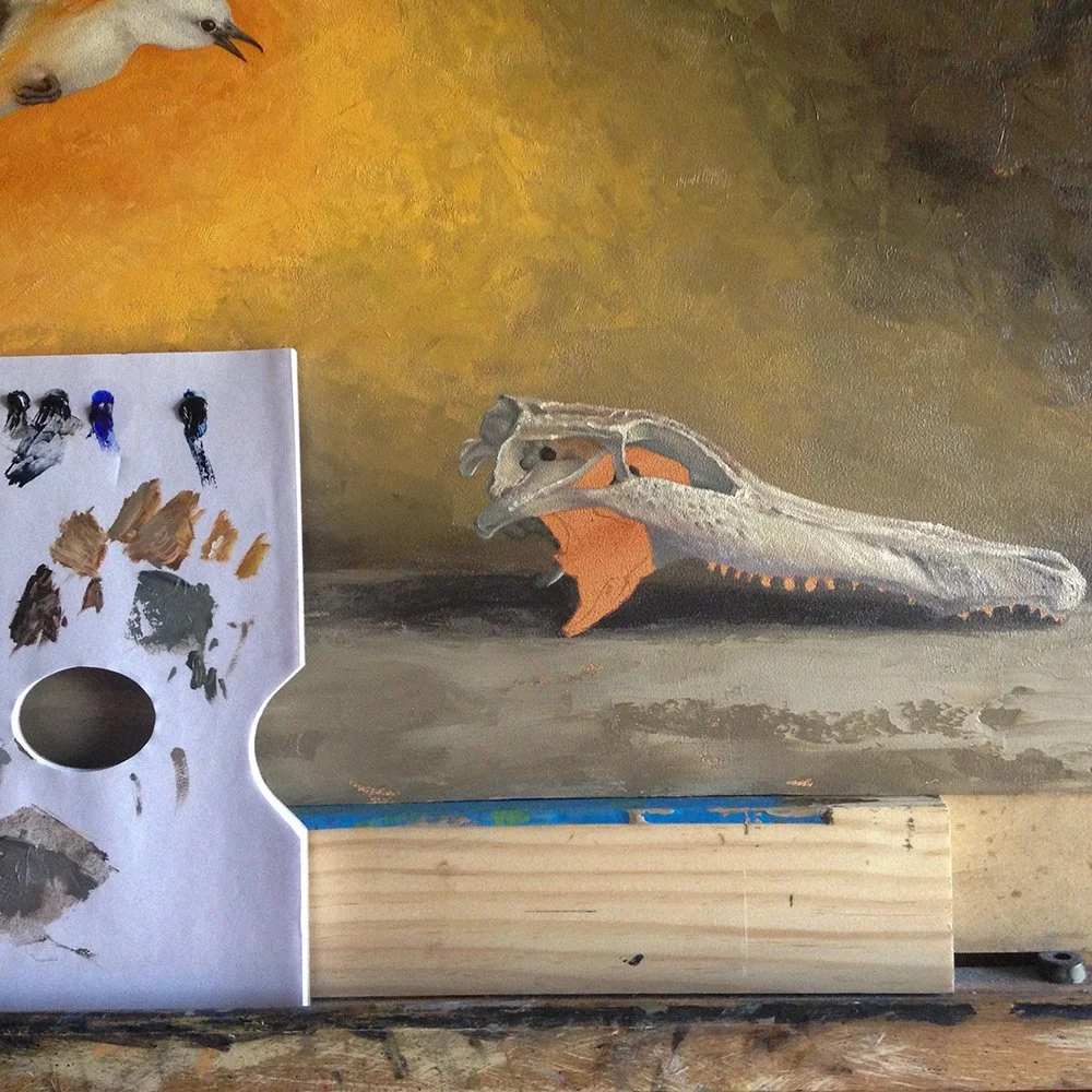 Painting of an alligator skull in progress with a painter's palette and paint swatches visible in the foreground.