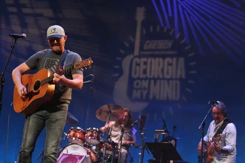 Musician playing guitar during a live performance on stage with a Georgia On My Mind sign in the background.