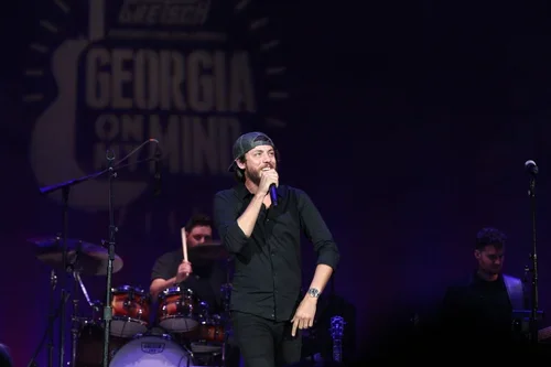 A man holding a microphone on stage during a performance with a band, with a 