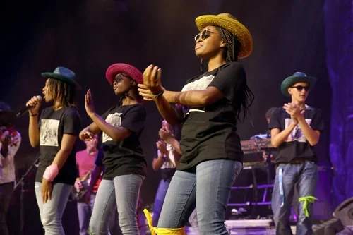 Group of women performing on stage, wearing colorful hats and sunglasses.