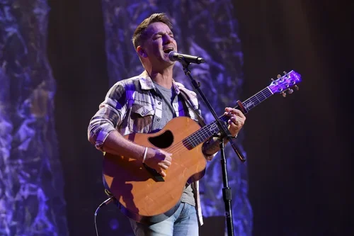 A man playing an acoustic guitar and singing into a microphone on stage.