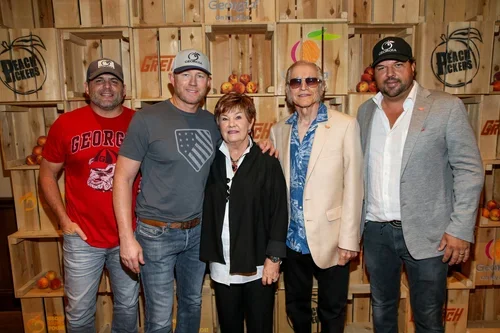 Five people standing together in front of wooden crates filled with oranges, with Peach Pickers branding visible, at a music or event setting.