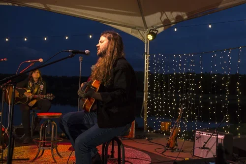 Two musicians performing under a canopy at sunset, with string lights in the background