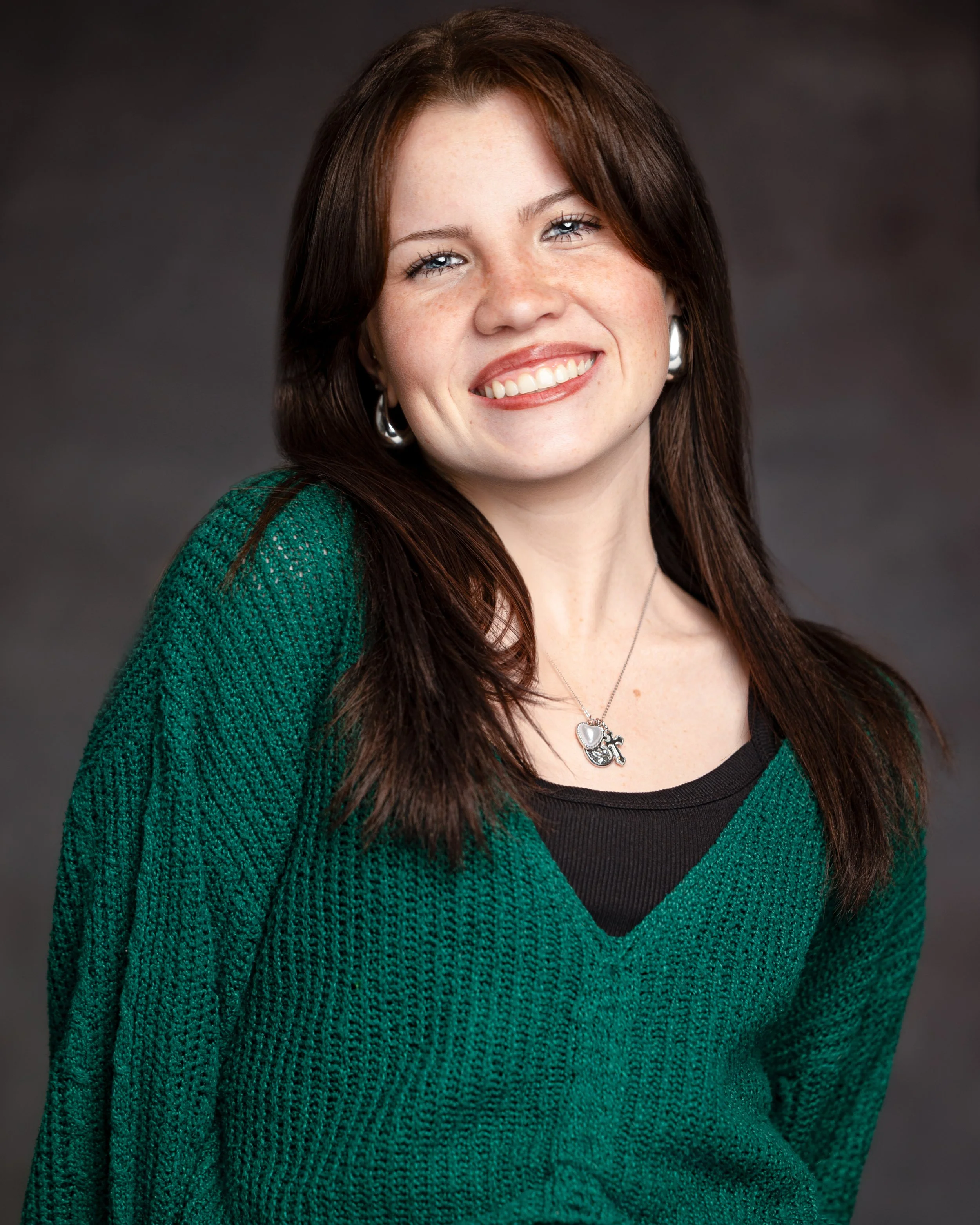 Black and white artistic dramatic headshot portrait of an opera singer with long, wavy hair wearing a dark top, looking at the camera.