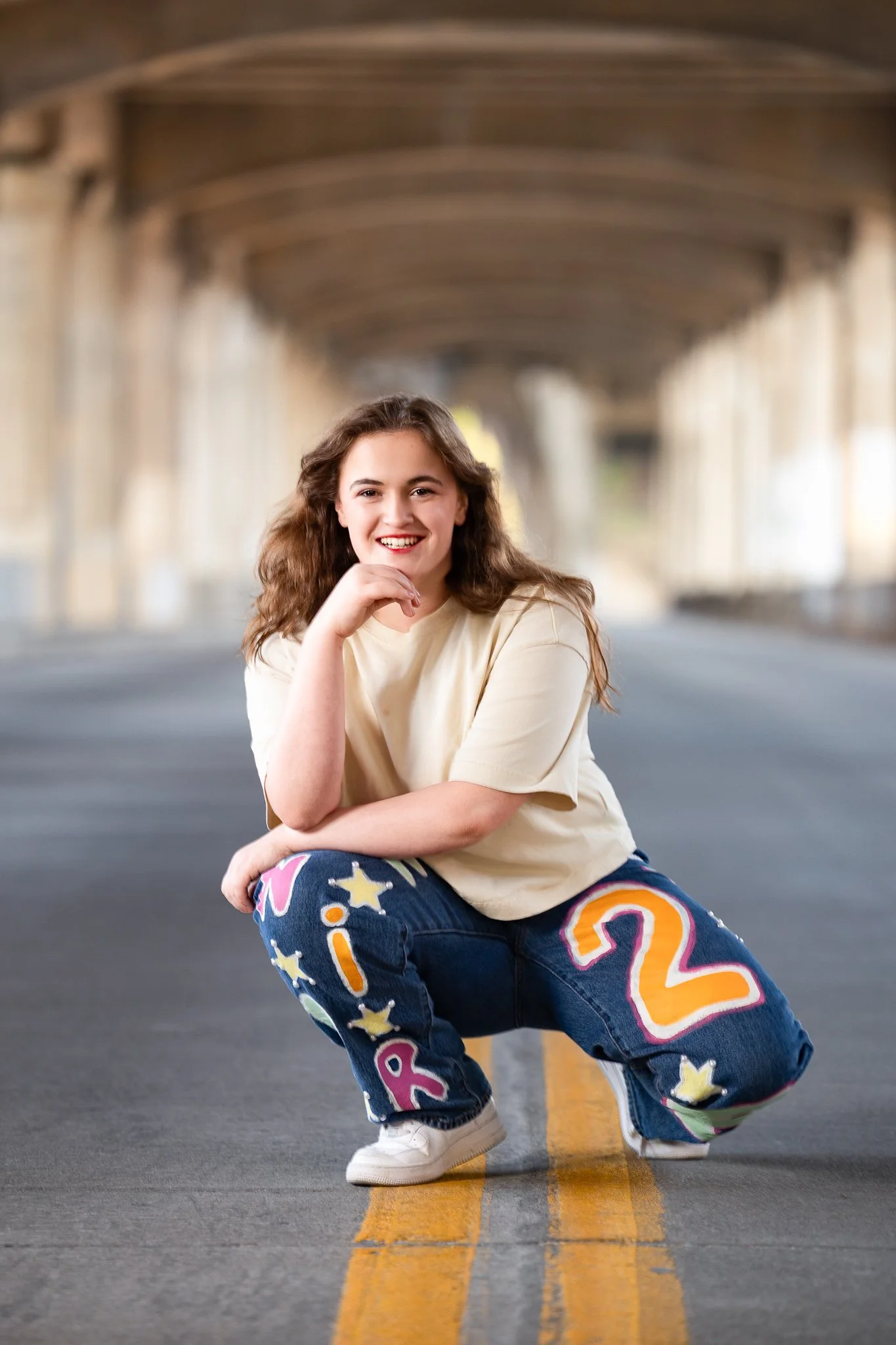 Editorial senior photo of a girl jumping and dancing on a Kansas City street with parked cars and buildings in the background.