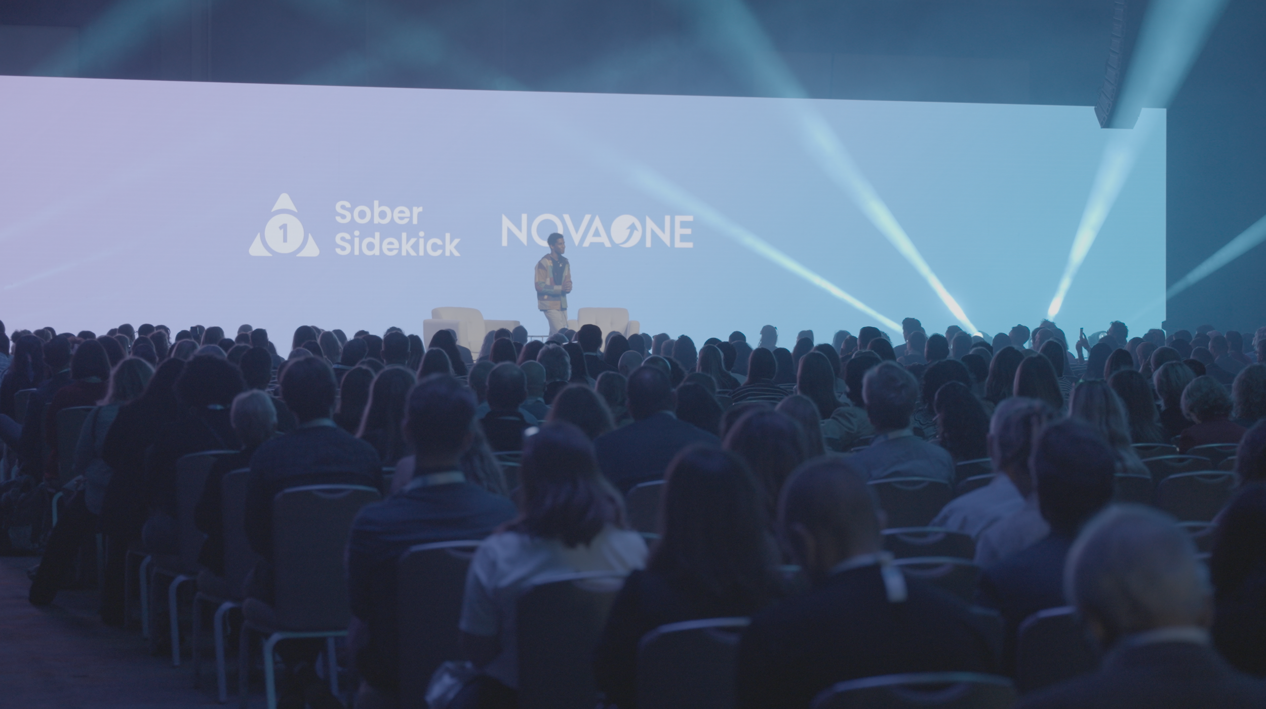 Large conference audience facing keynote stage with screen and stage lighting — Orange County event video production