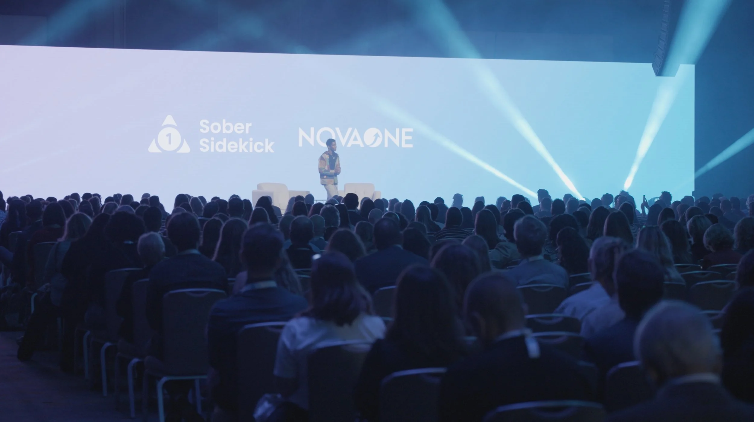 Live event videography of keynote speaker on stage at corporate conference with projected branding and stage lighting