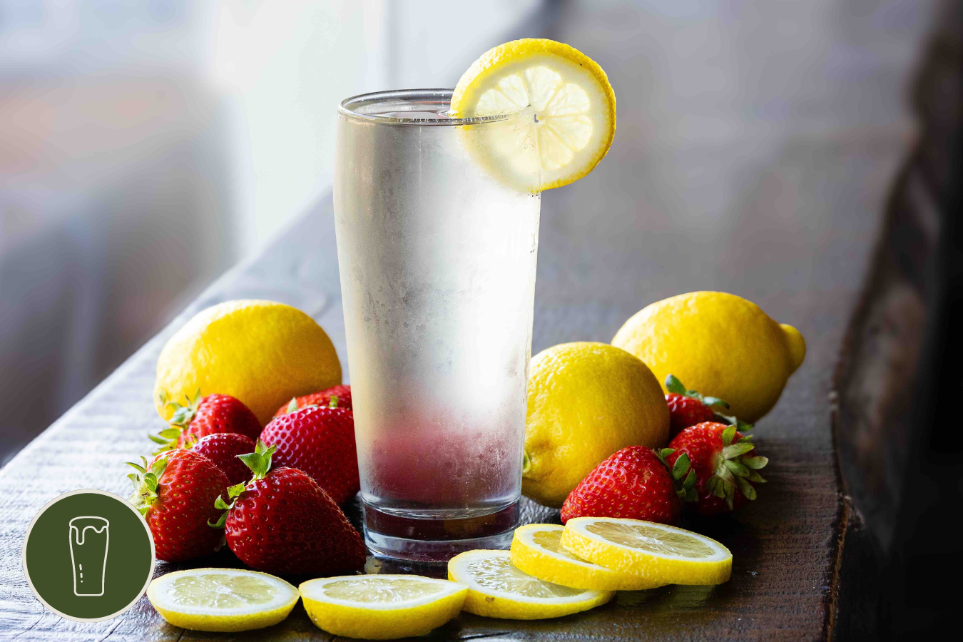 Pint of pontoon party seltzer surrounded by strawberries and lemons on a wooden bar