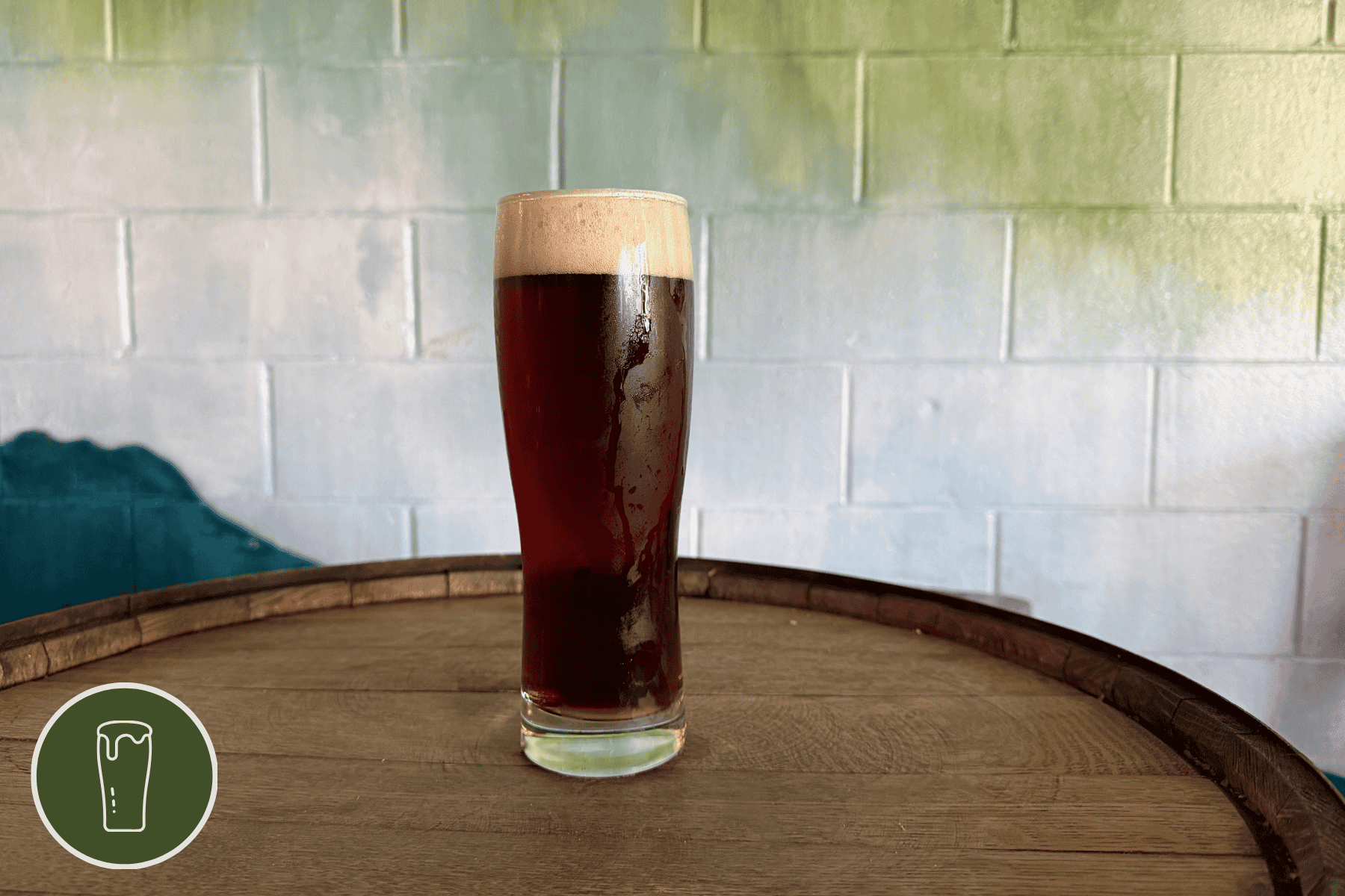 Lager glass of Shred By Night on a wooden barrel in front of a painted wall