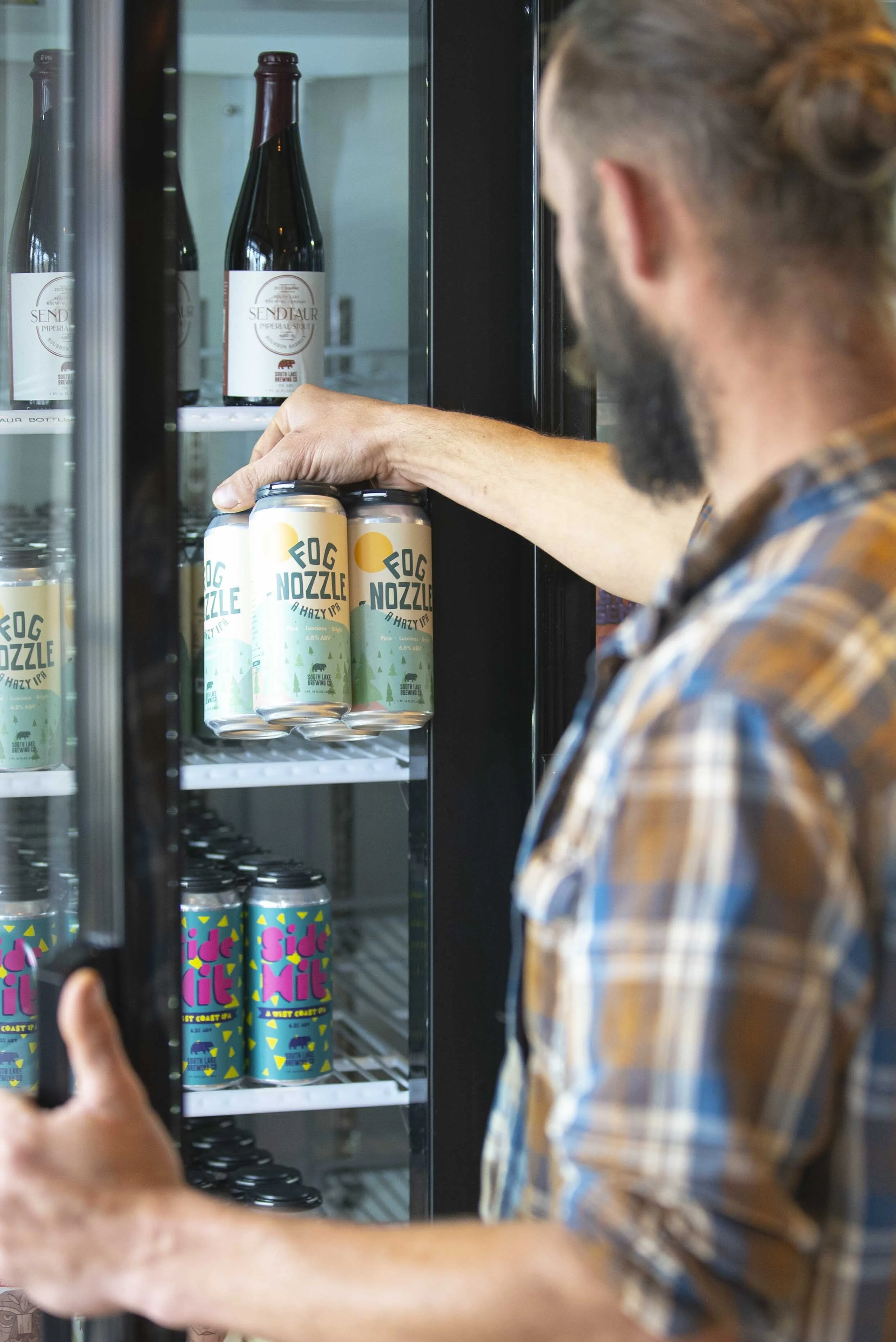Man opening a fridge and holding a 4-pack of Fog Nozzle Hazy IPA