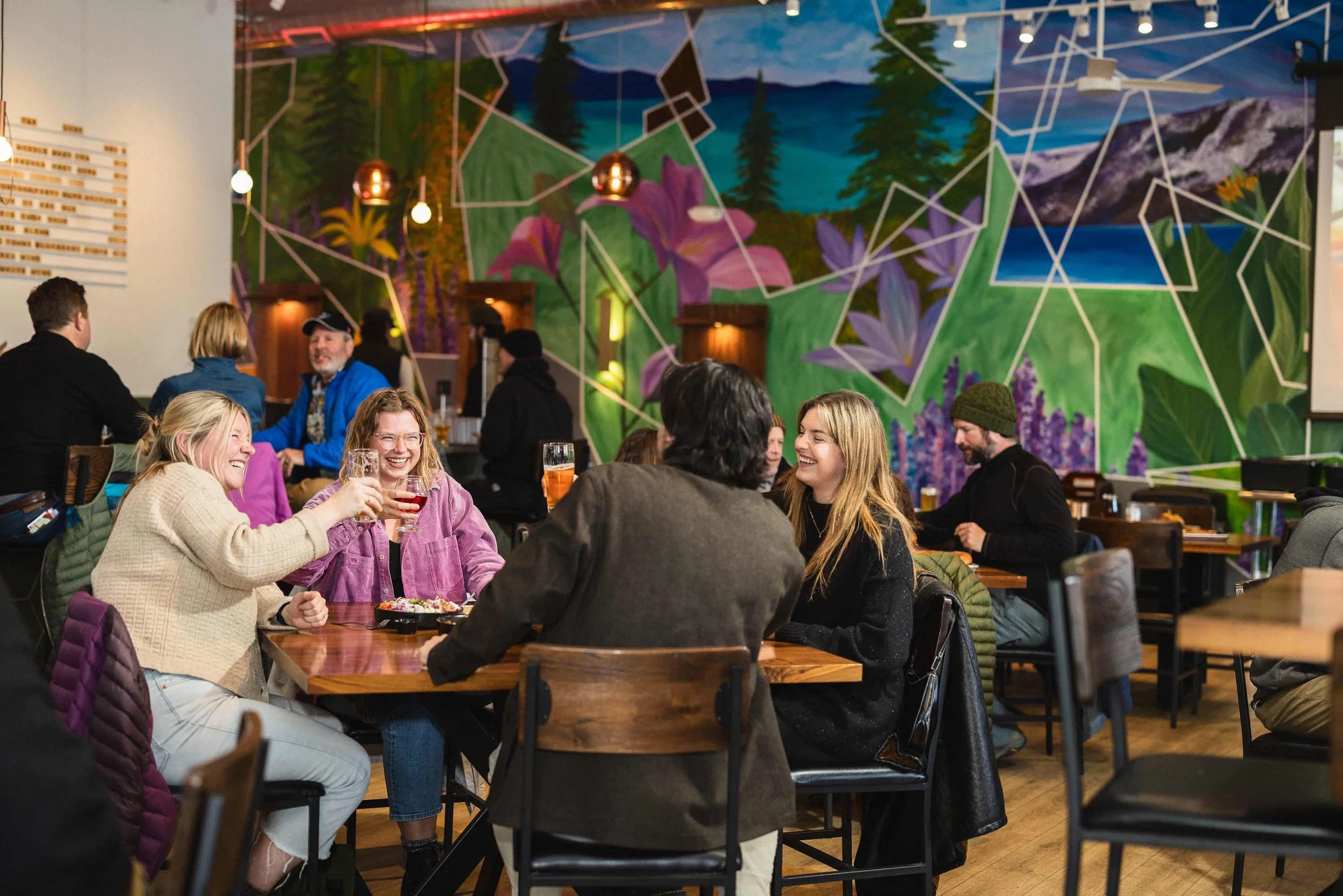 Group of people cheers with beers in front of a mural