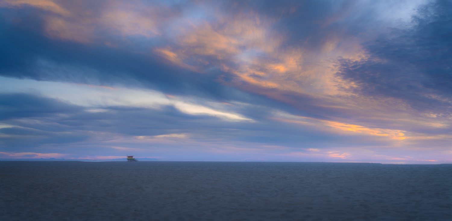A vast ocean with a distant oil rig and a colorful sky with clouds during sunset or sunrise.