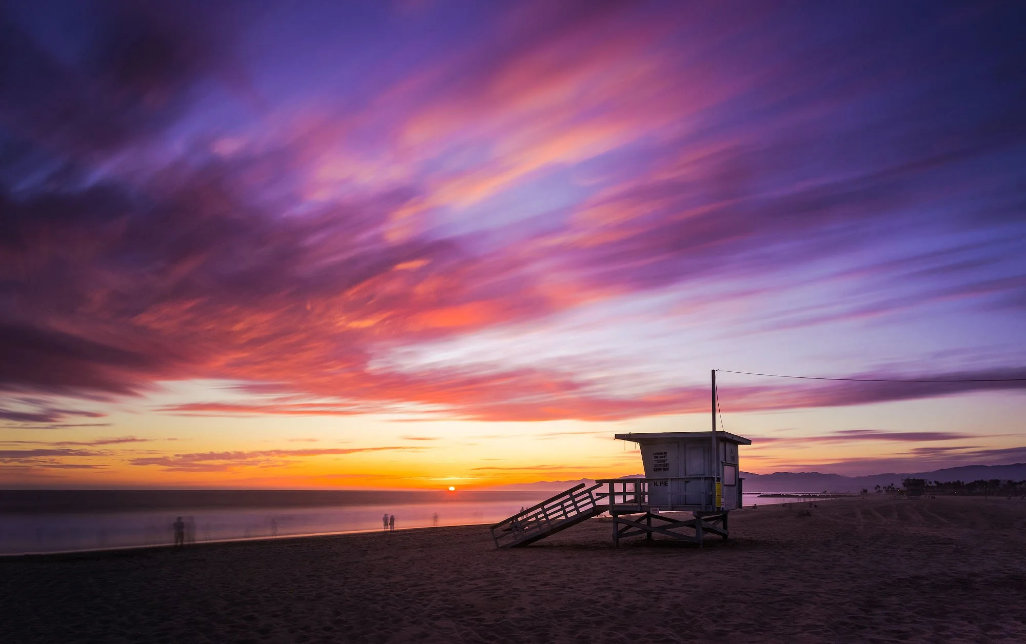 Colorful sunset sky over a beach with a lifeguard station in the foreground.