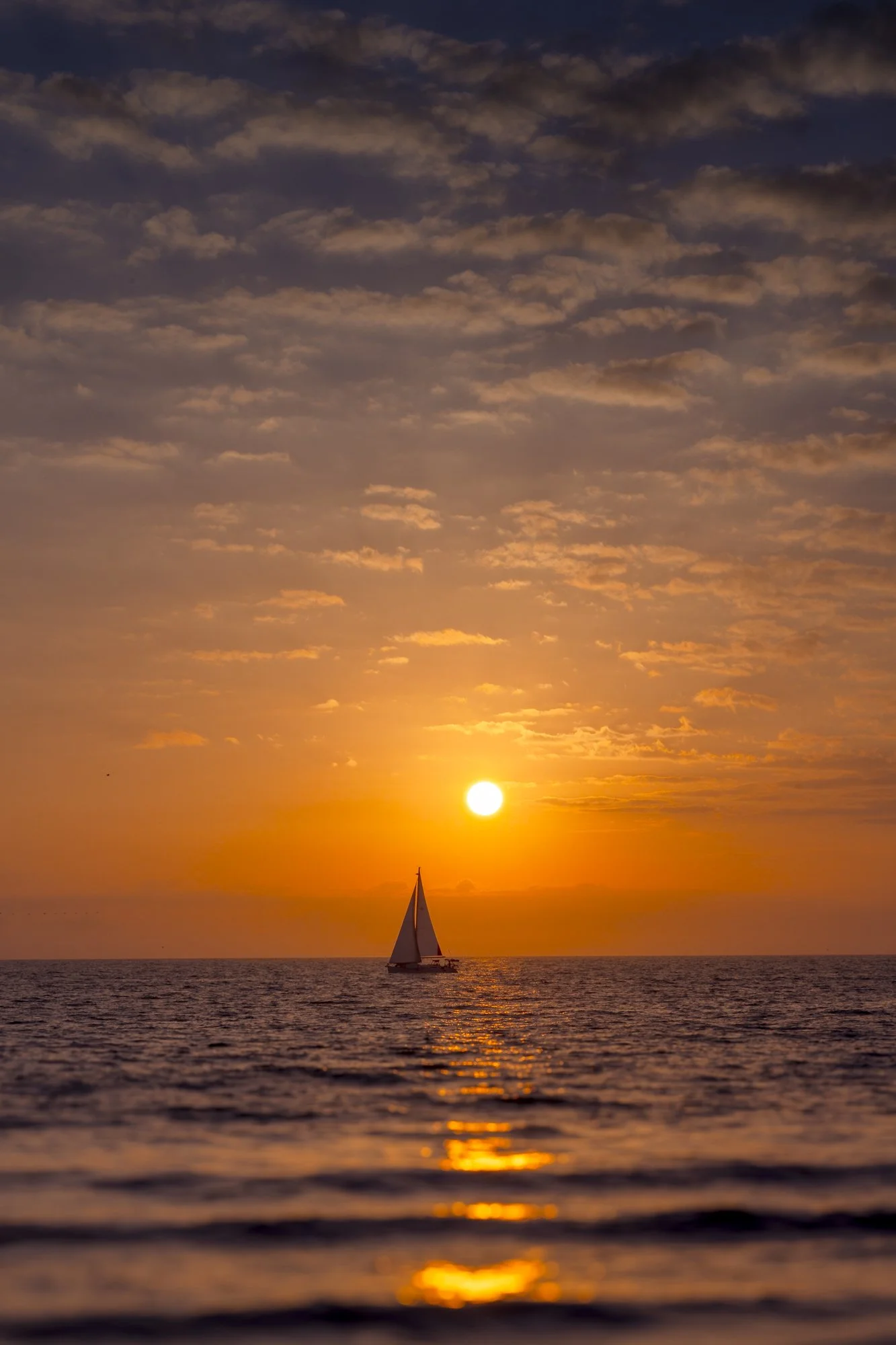 Sailboat on the ocean during a sunset with a colorful sky and scattered clouds.