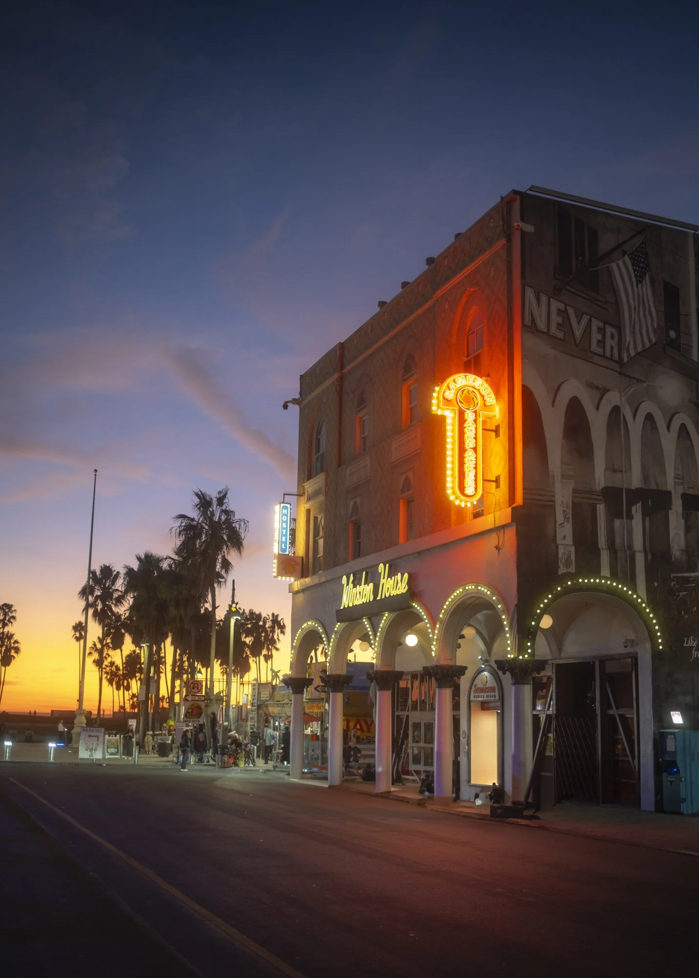 Sunset view of the Muscle Beach House with neon signs and palm trees on Santa Monica Pier in California.