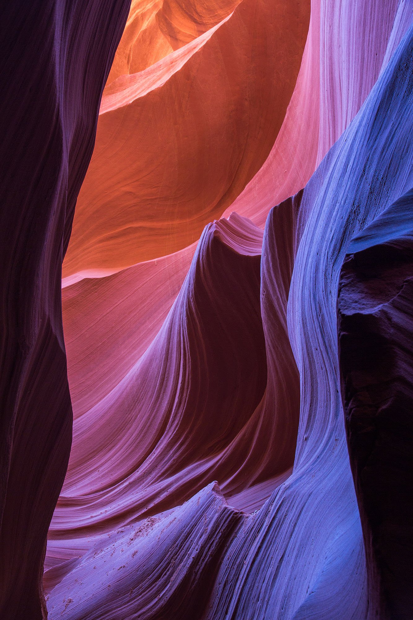 Colorful sandstone canyon with smooth, winding walls in shades of purple, pink, orange, and blue.