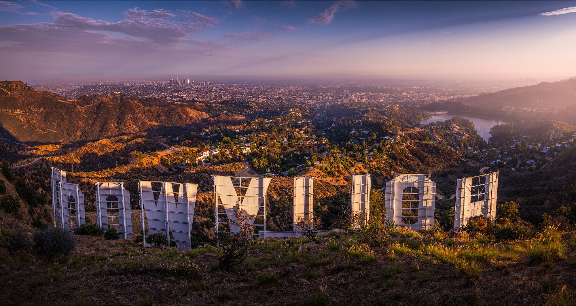 The Hollywood Sign on a hillside overlooking Los Angeles during sunset with a cityscape in the distance.