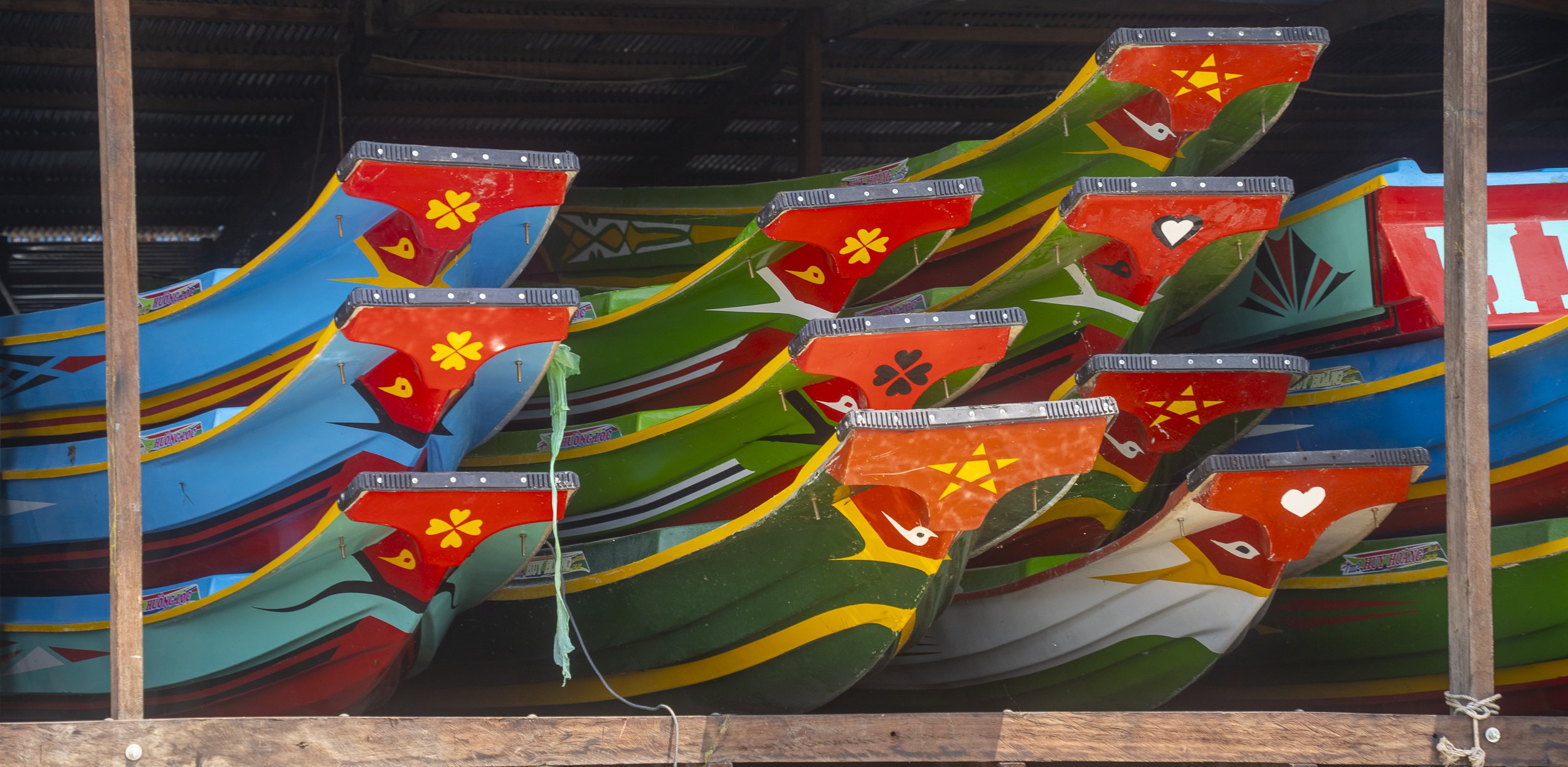 Colorful traditional wooden boats stacked in a covered shed, painted in vibrant colors and patterns.