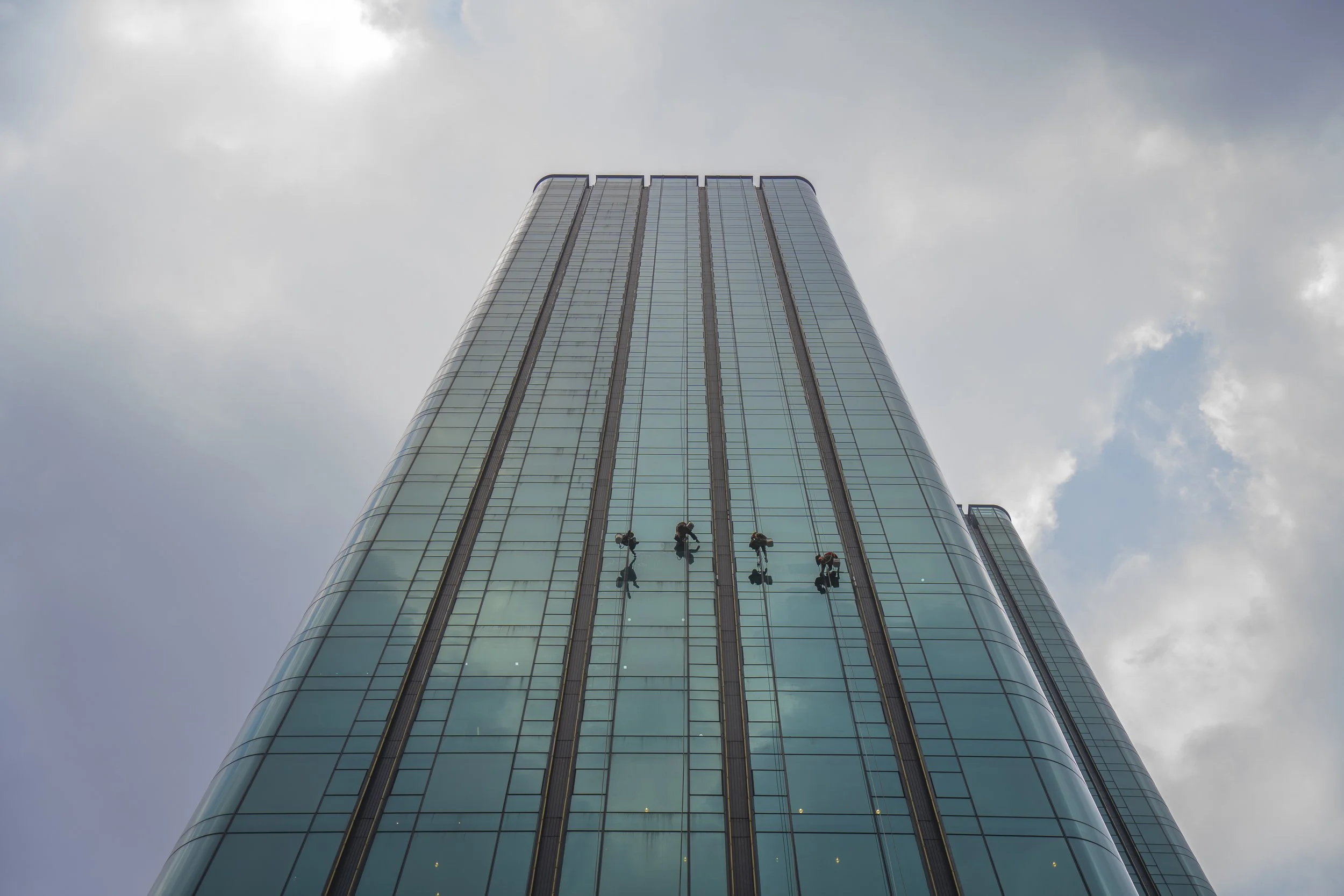Workers cleaning the glass windows of a tall modern skyscraper during the day