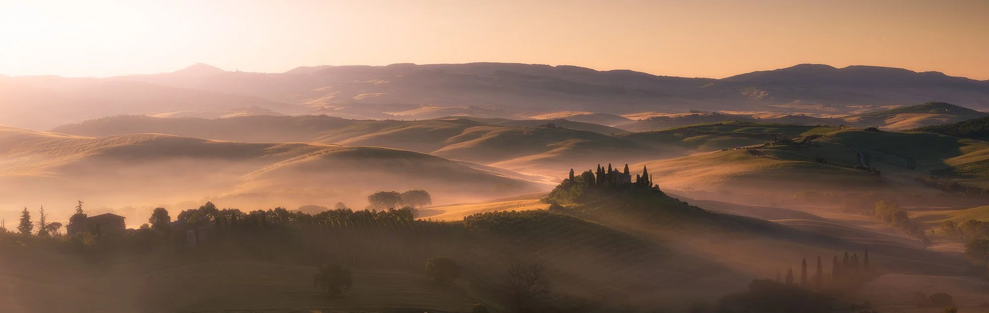 Golden hills and valleys at sunrise with a small castle and cypress trees on a hilltop in Tuscany, Italy.