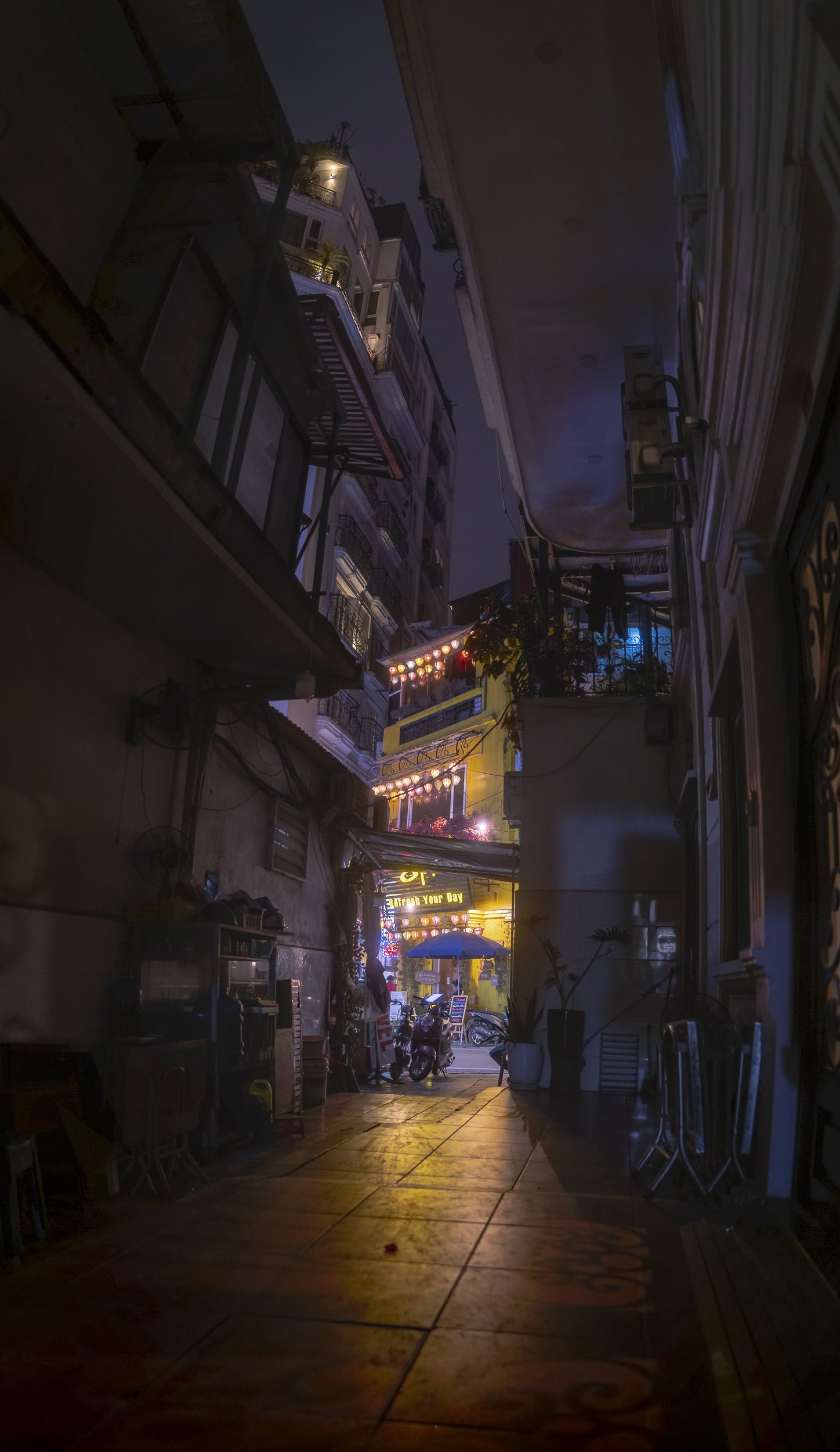 Nighttime alleyway with closely packed buildings, illuminated signs, and decorative string lights.