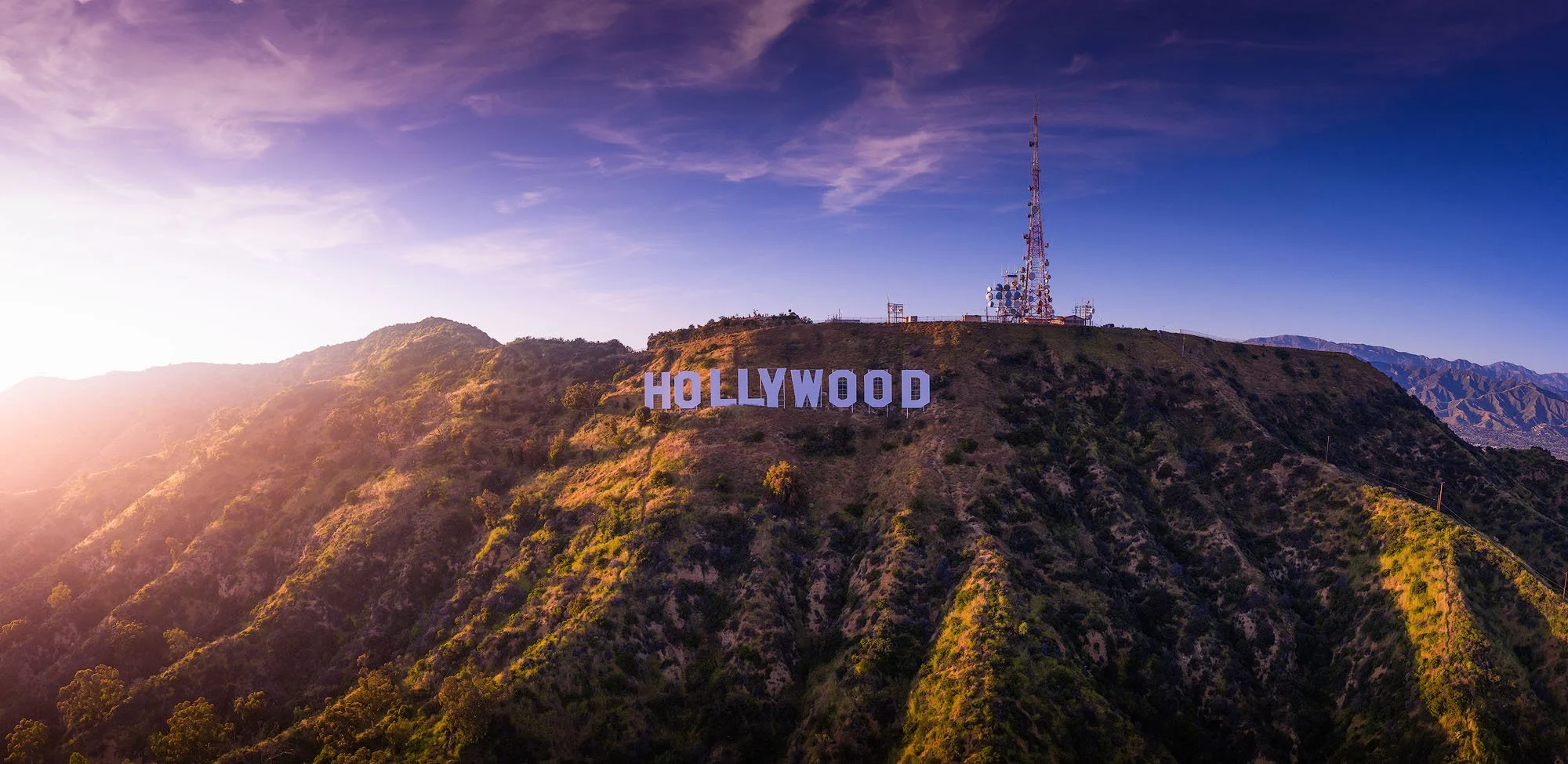 The Hollywood sign on a hillside at sunset with antennas on the hilltop.
