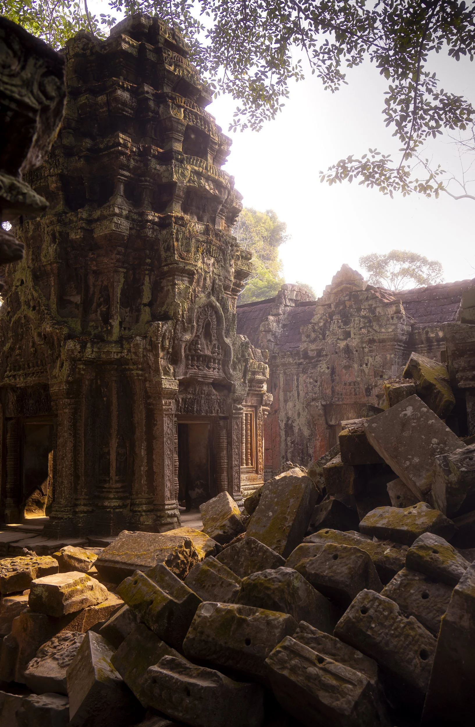 Ancient stone temple ruins with intricate carvings, fallen stones, and dense greenery in the background.