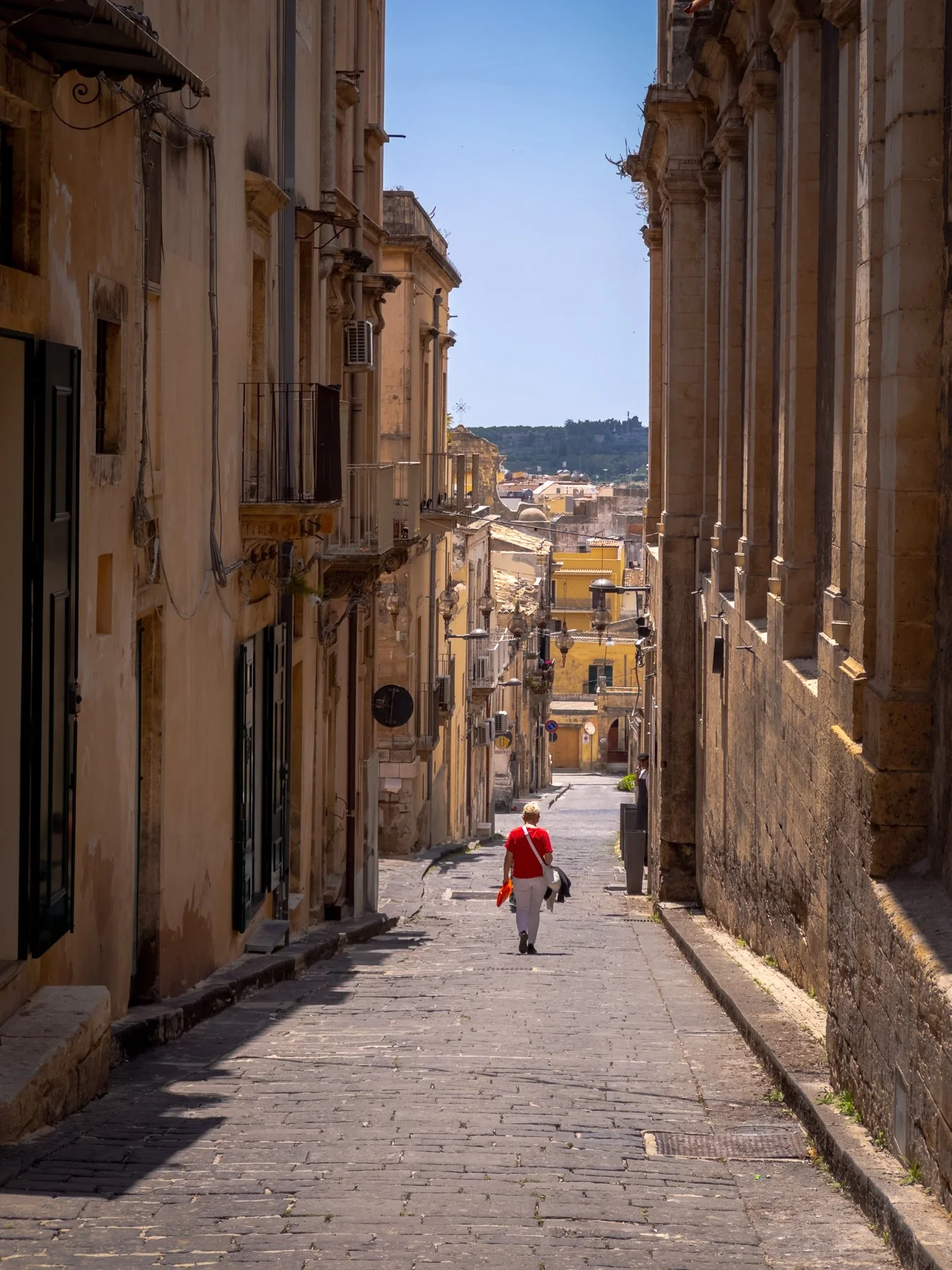 A person walking down a narrow cobblestone street lined with old, weathered buildings in a historic European city during daytime.