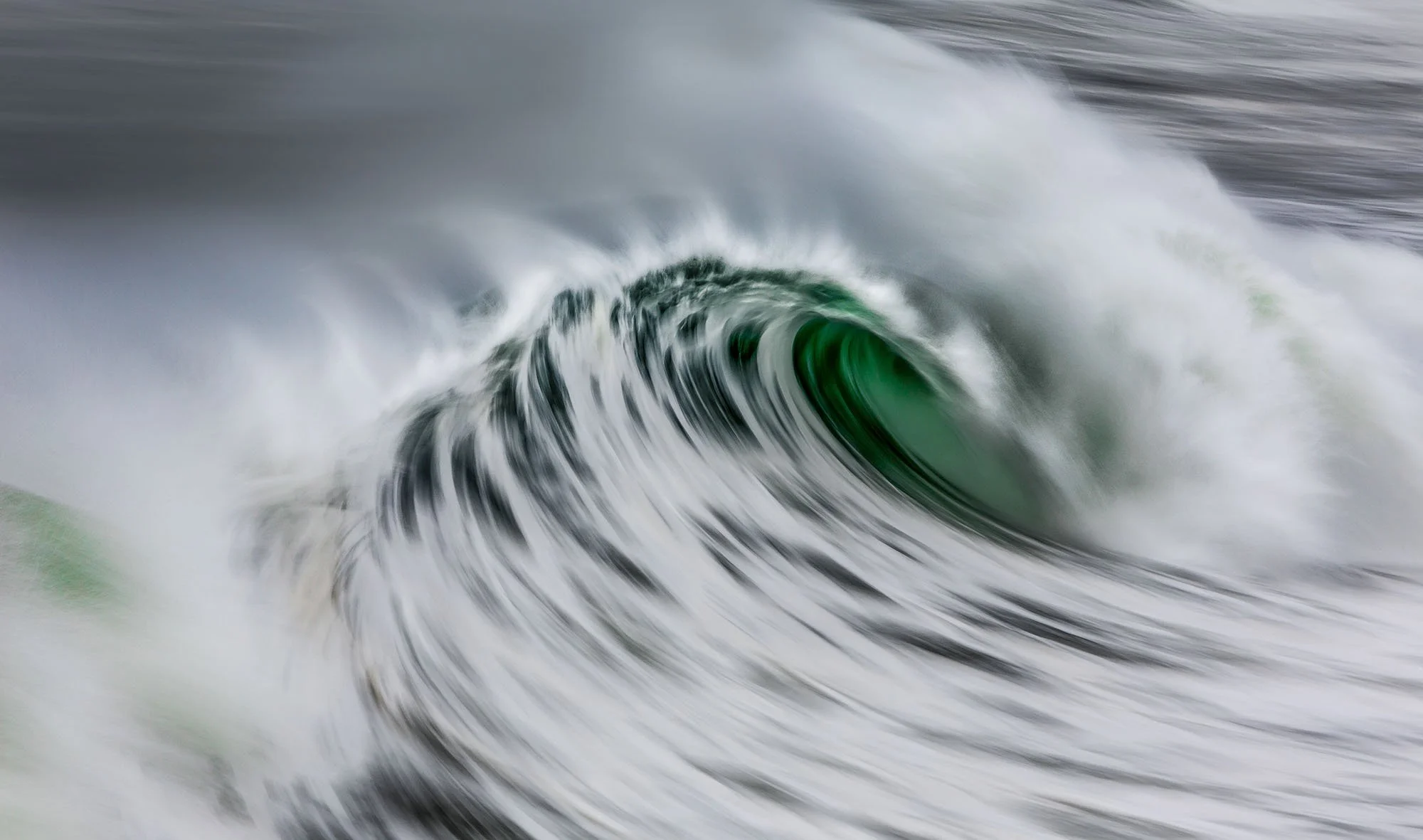 A large wave curling and crashing in the ocean with white foam and a green interior