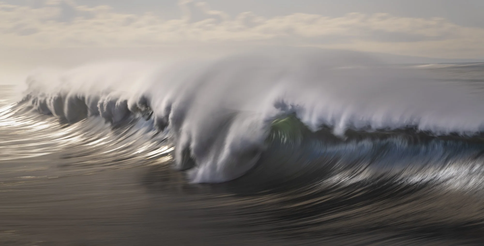 Large ocean wave crashing with white spray and a partly cloudy sky