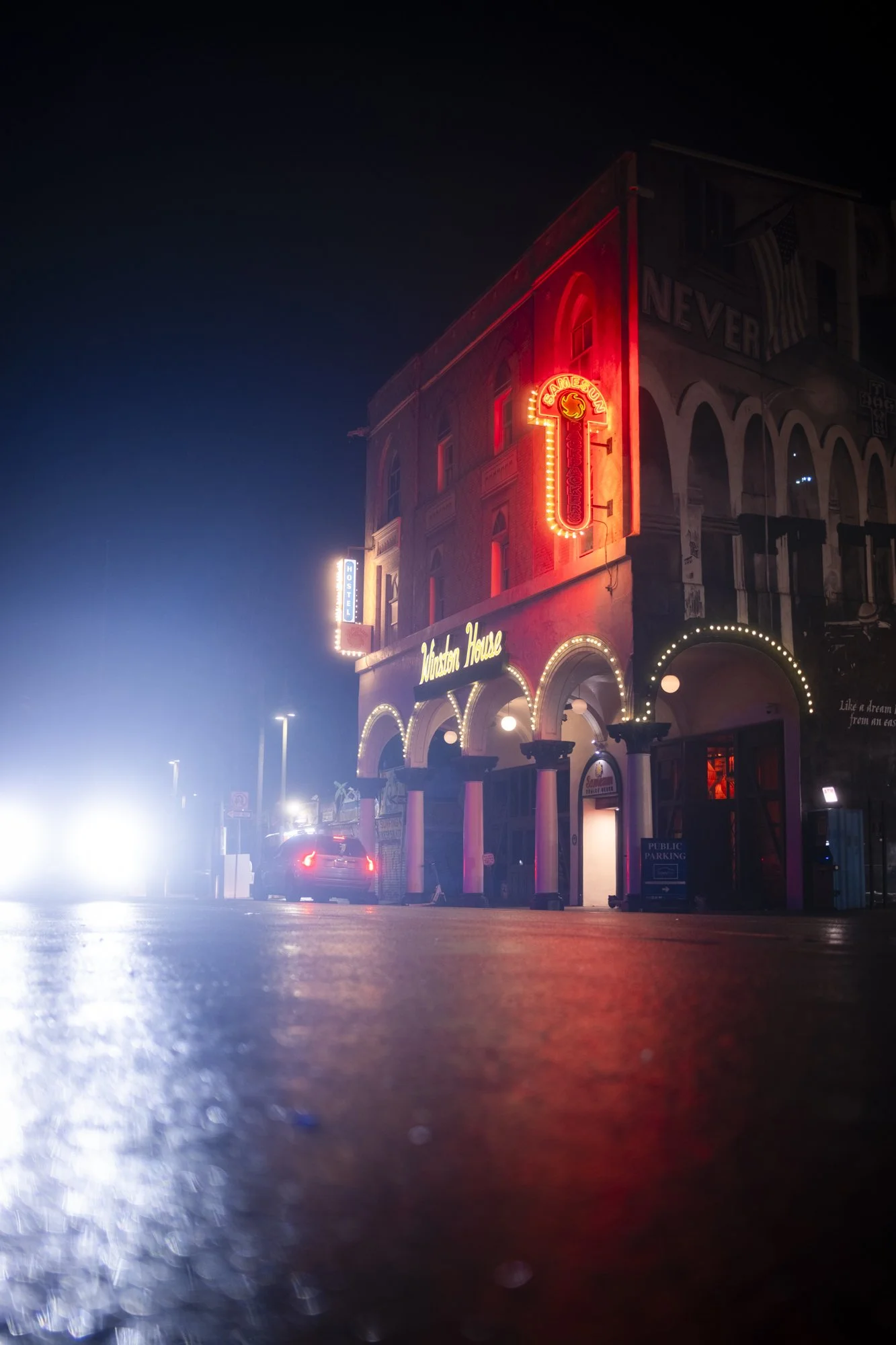 Night view of a building with neon signs reading 'Cameo' and 'Western House,' illuminated archways, and a parked car on the street with fog or mist.